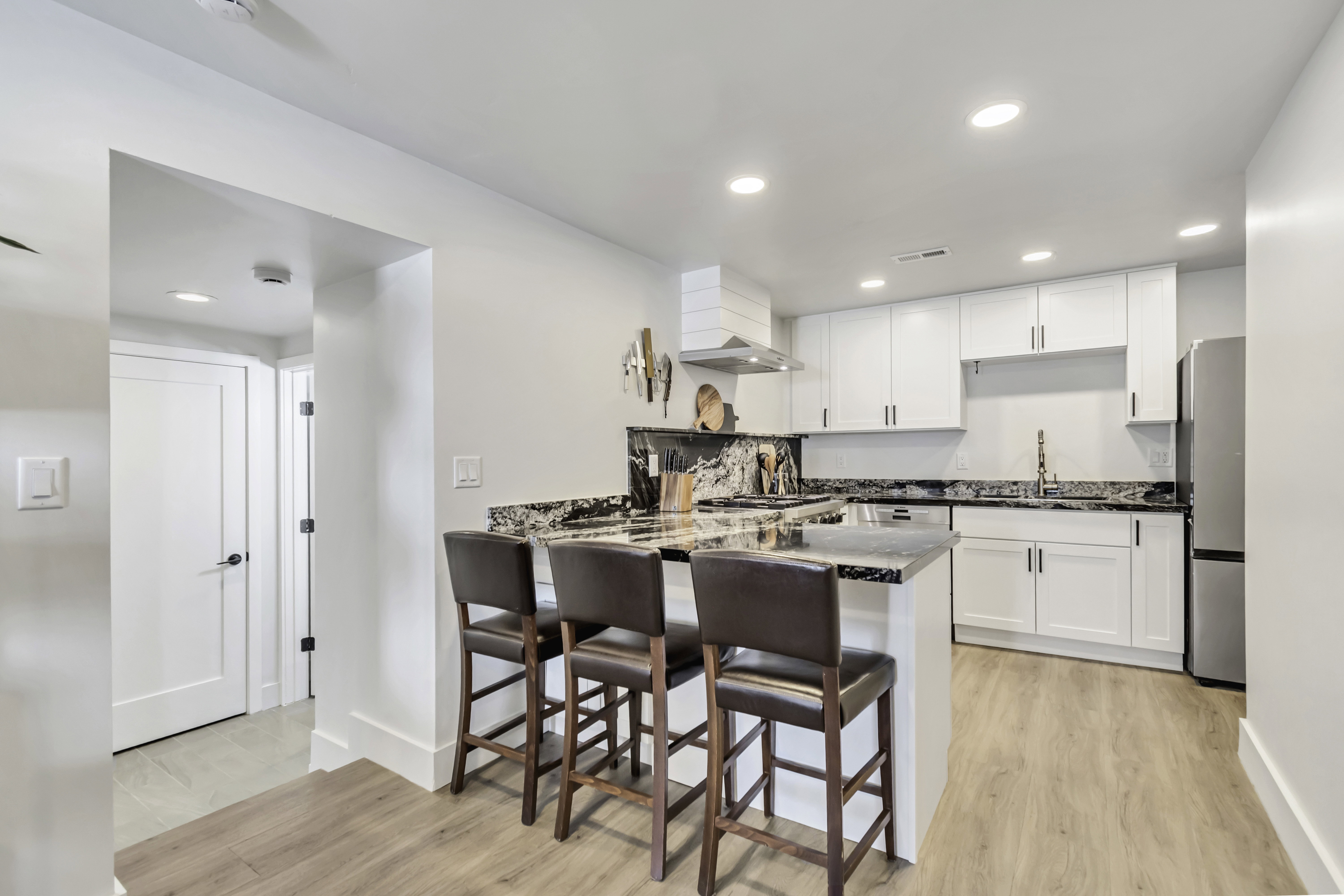 Modern kitchen featuring white cabinetry, stone countertops, a stainless steel refrigerator, and wood-finish flooring