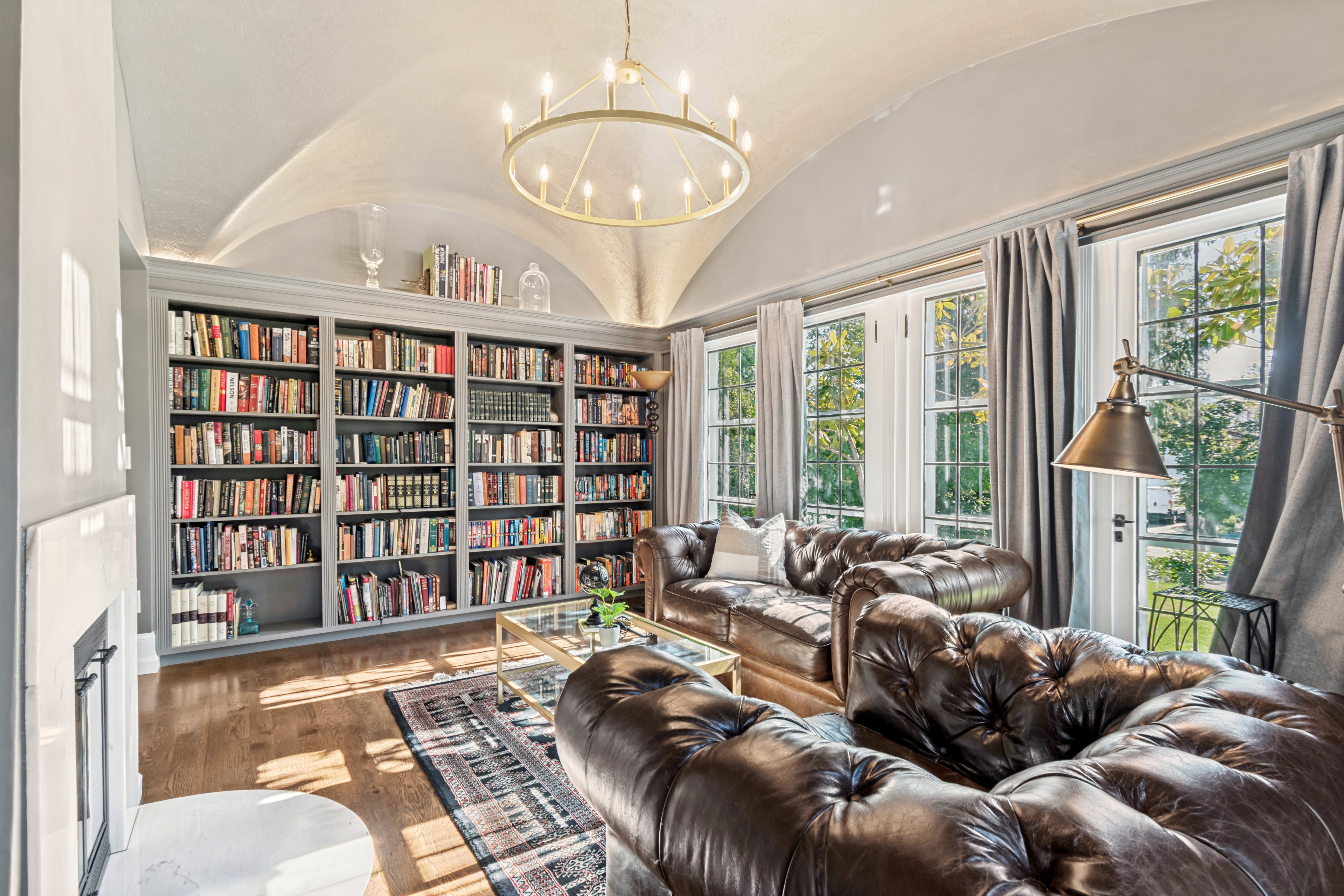 Vaulted ceiling with a central chandelier, extensive built-in shelving, hardwood flooring, and multiple windowed doors