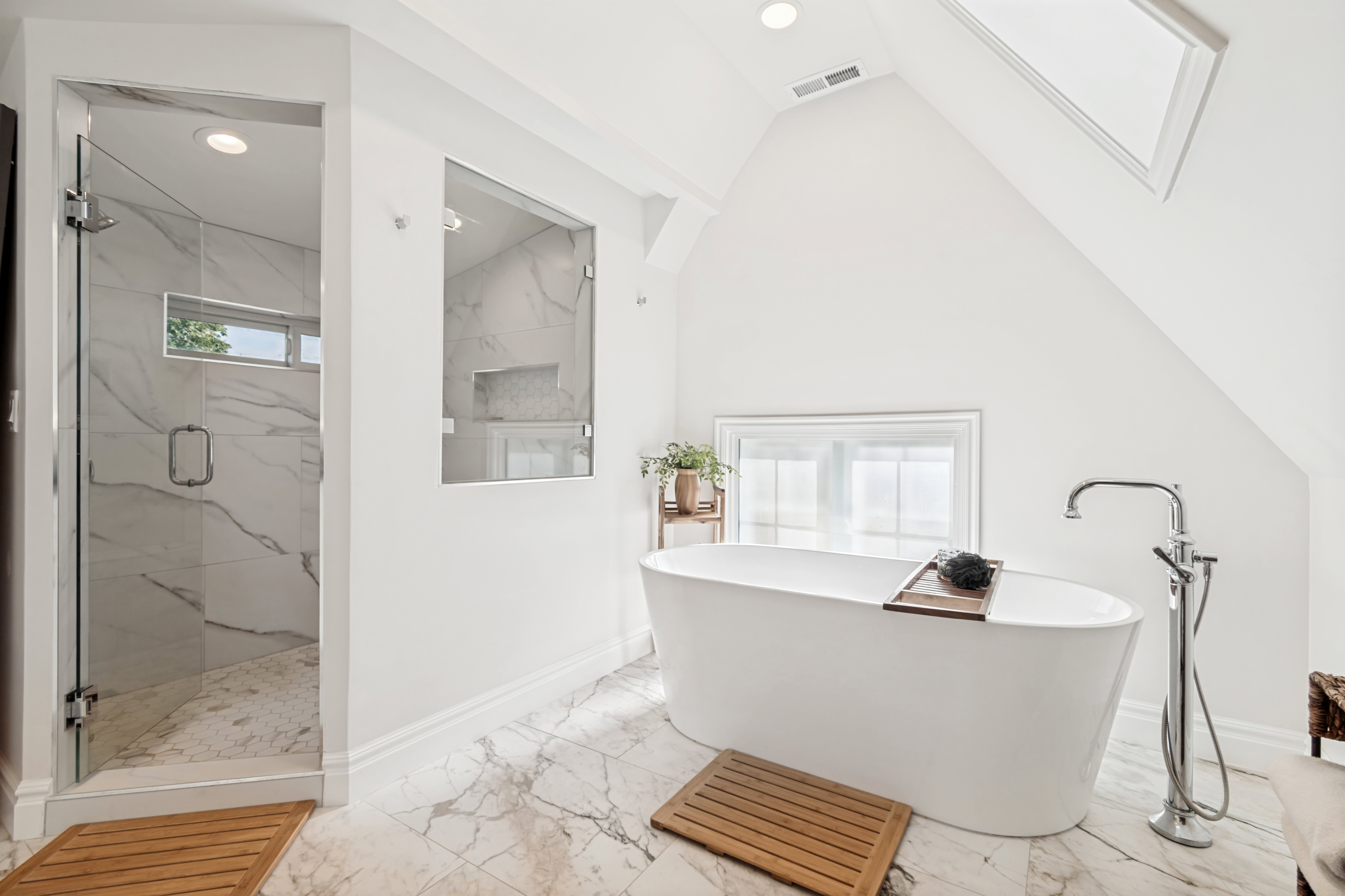 Freestanding soaking tub with floor-mounted faucet, complemented by a glass-enclosed shower with marble-look tile
