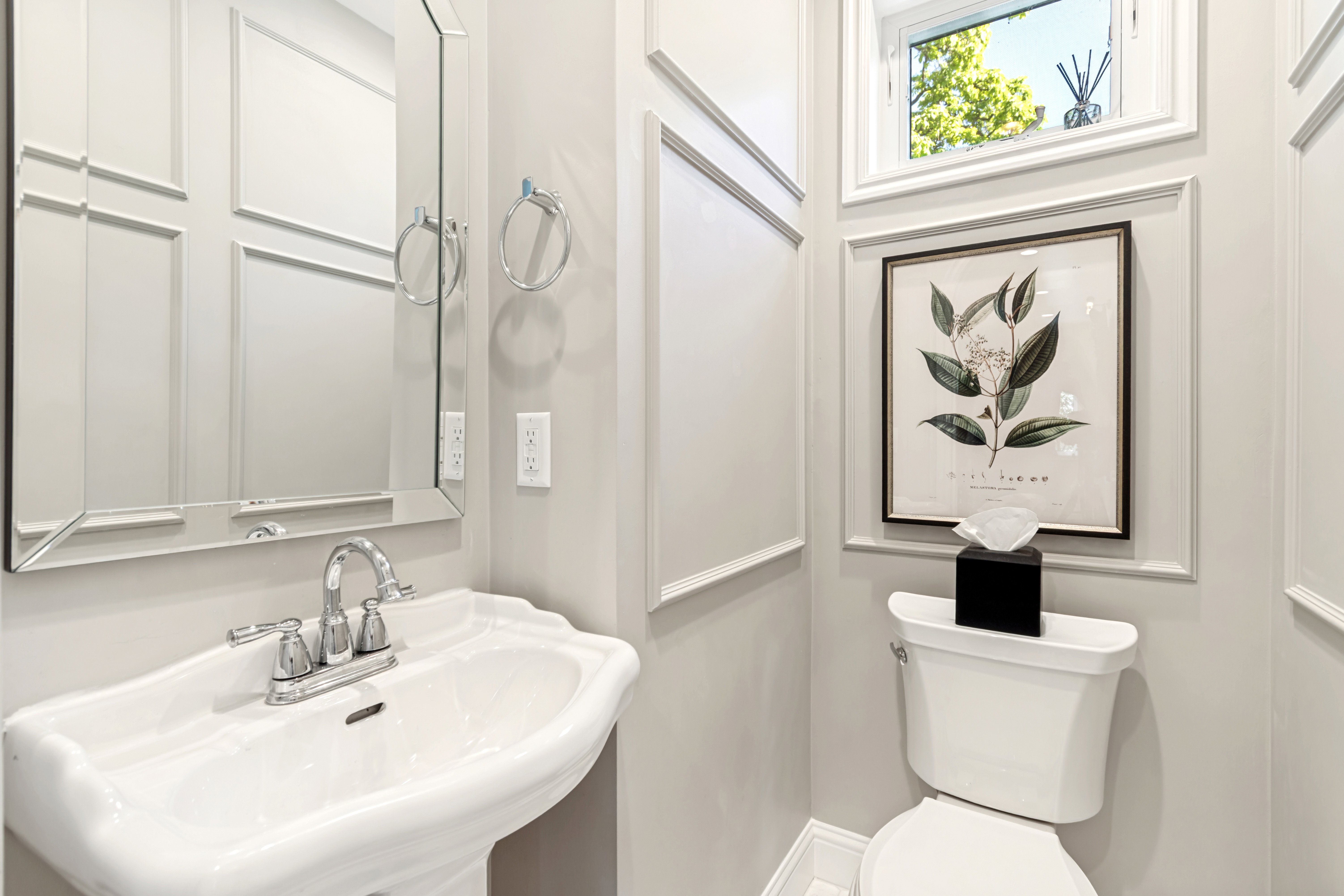 Pedestal sink with chrome faucet, framed mirror, and wainscoting details
