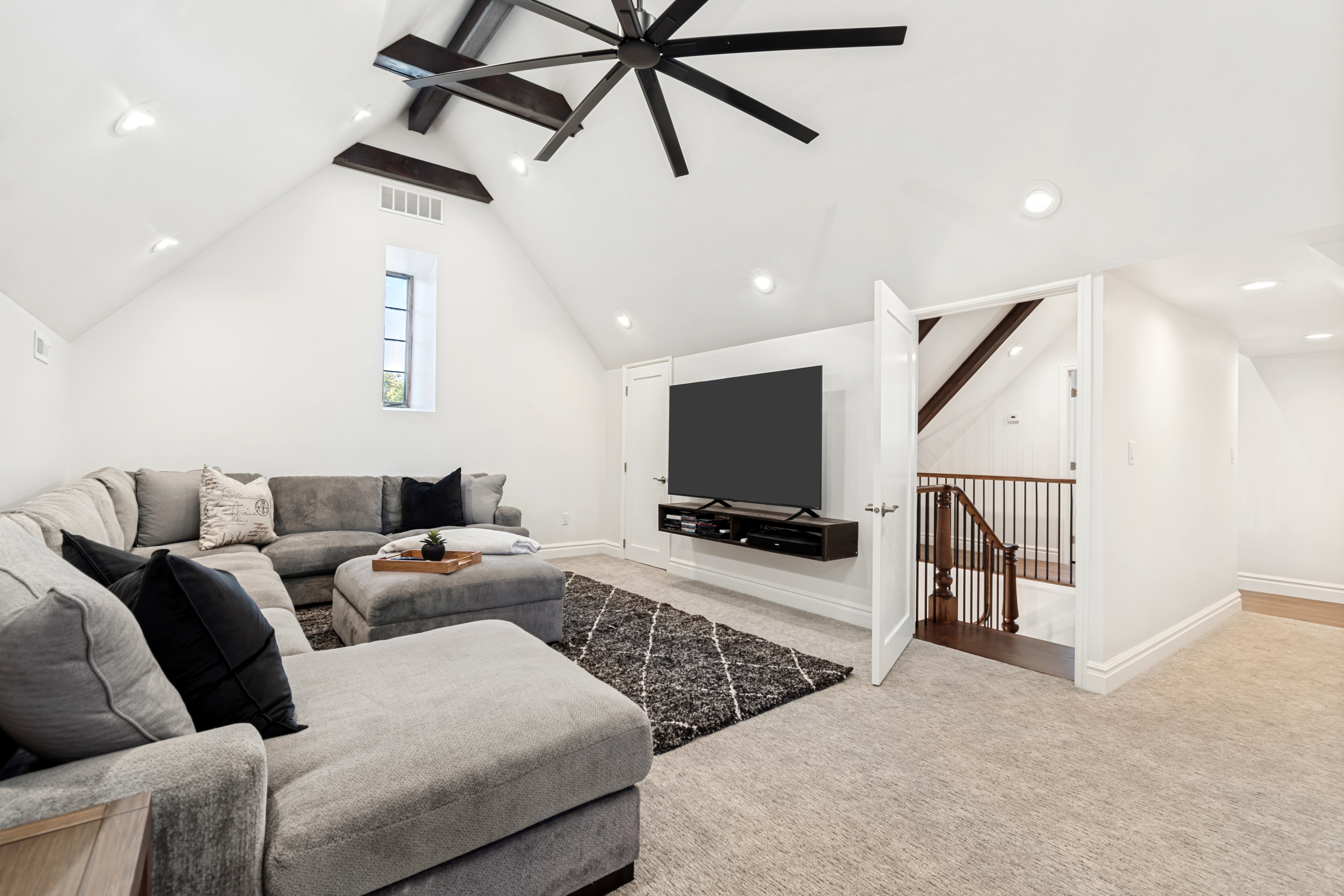 Vaulted ceiling room featuring exposed dark wood beams, recessed lighting, and a prominent dark-finish ceiling fan