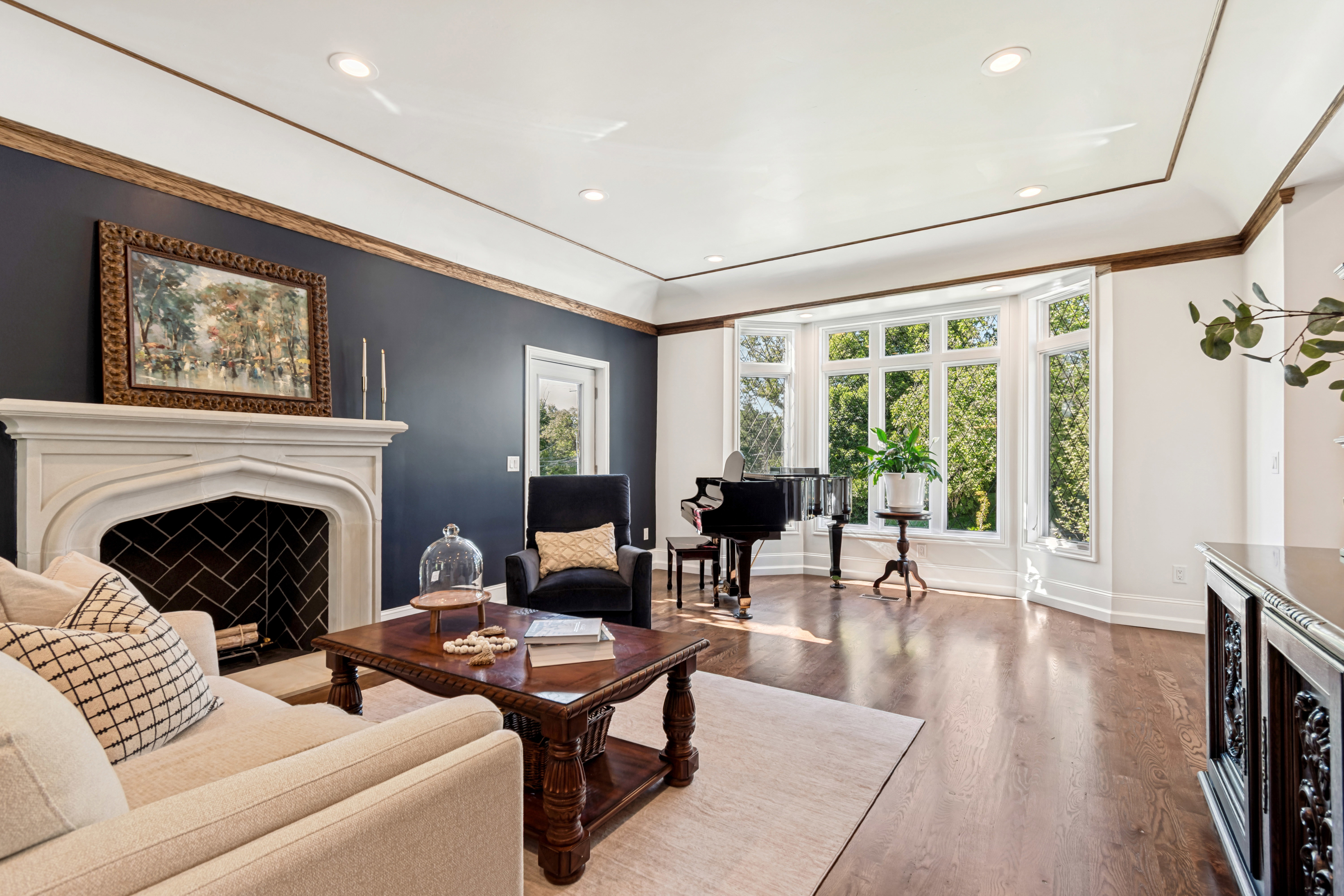 Spacious room featuring a stone fireplace with a herringbone-patterned firebox, a large bay window, recessed lighting, crown molding, and wood-finish flooring