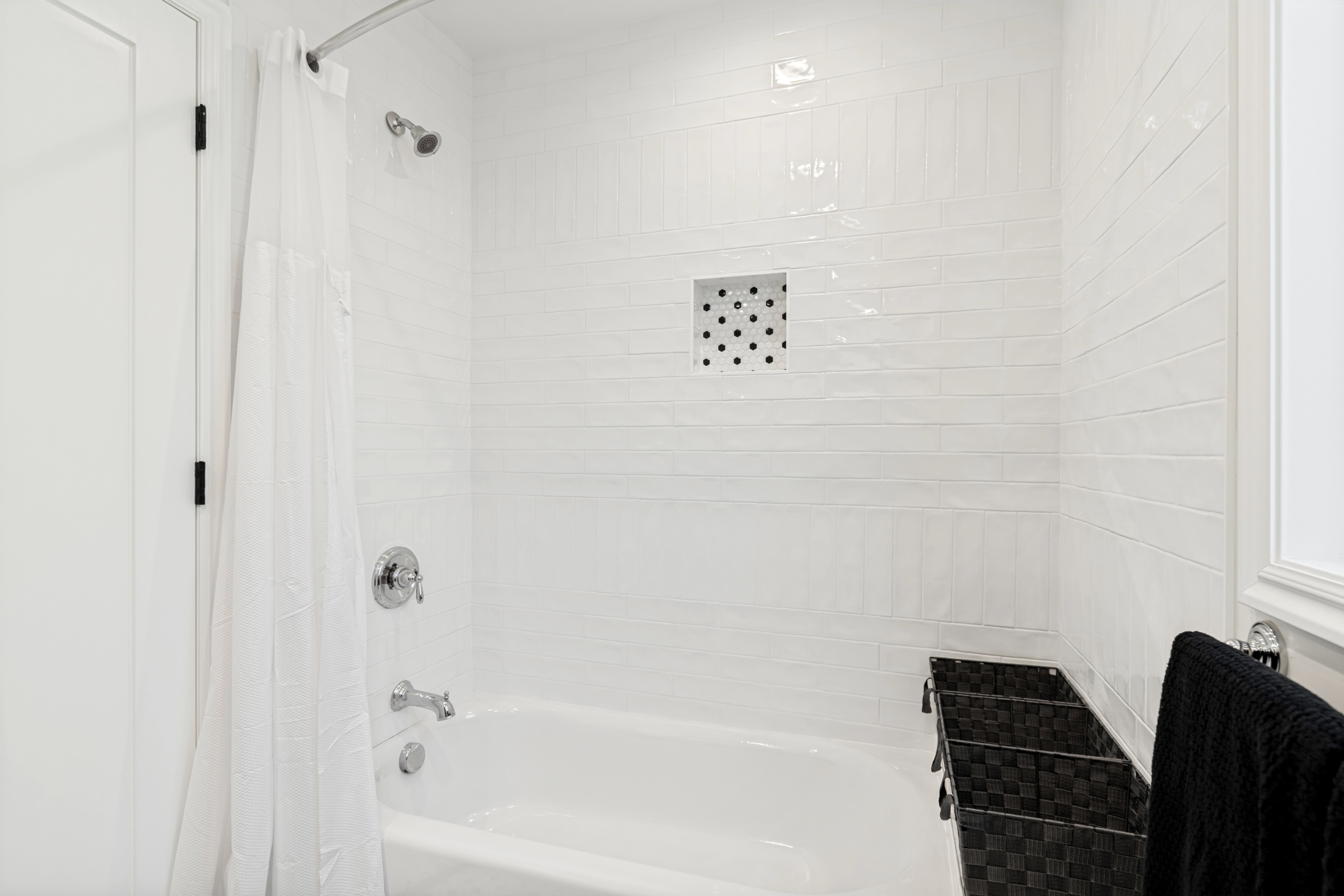 Bathtub with chrome fixtures, subway tile surround, and an integrated shower niche with mosaic tile accent