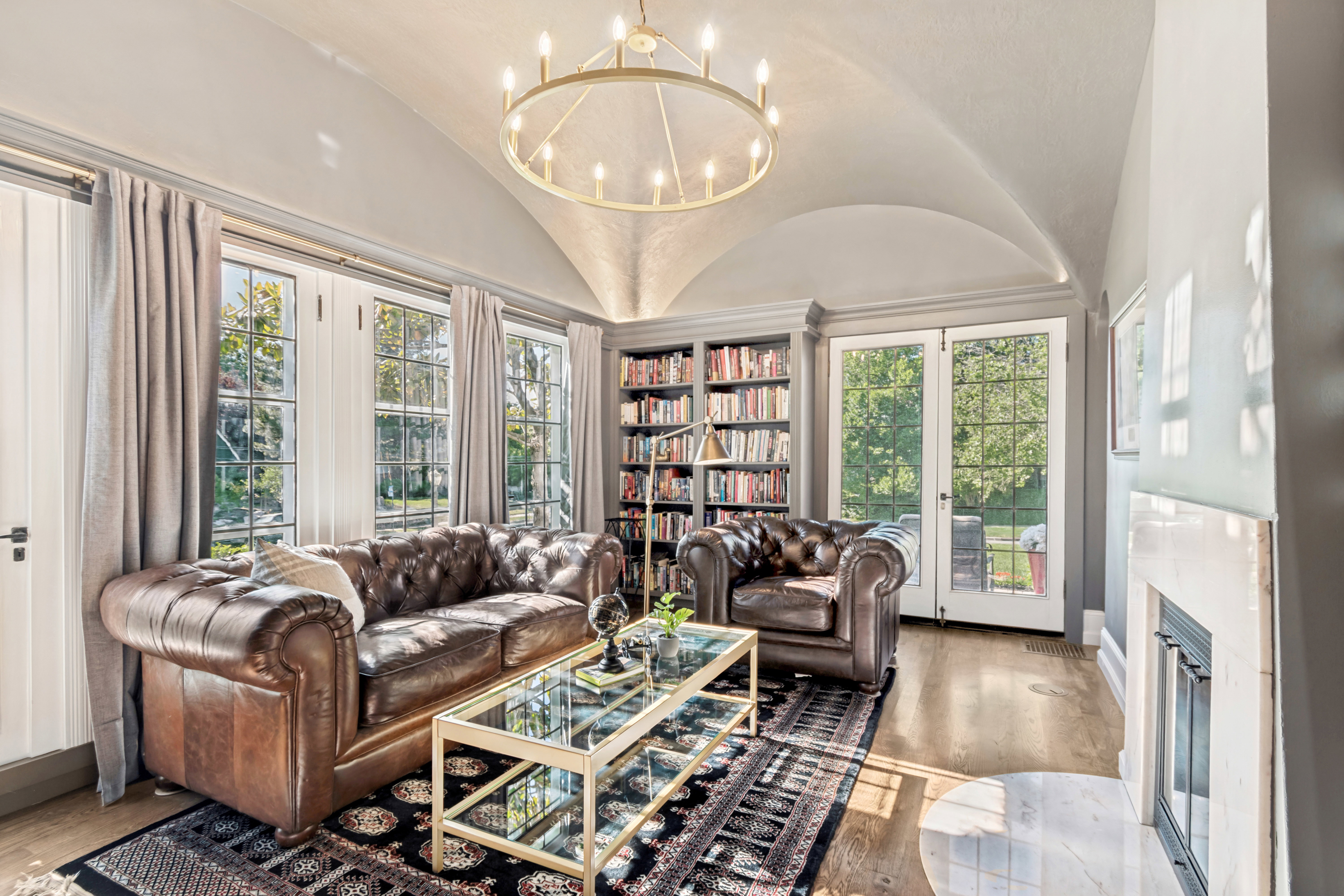 Vaulted ceiling featuring a circular chandelier, hardwood flooring, built-in shelving, fireplace with white surround, and multiple windowed exterior doors
