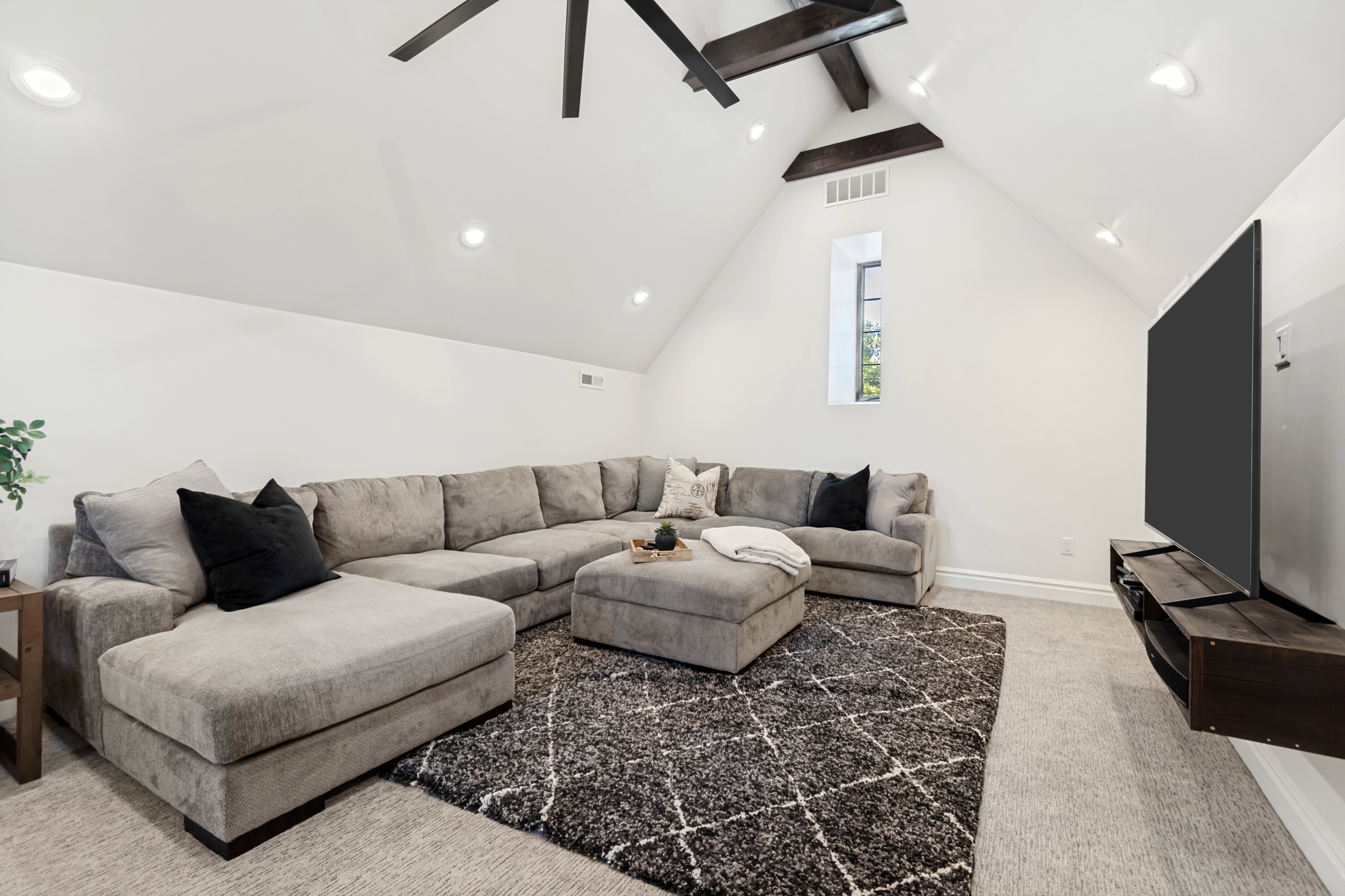 Vaulted ceiling room featuring exposed dark wood beams, recessed lighting, and a prominent dark wood ceiling fan