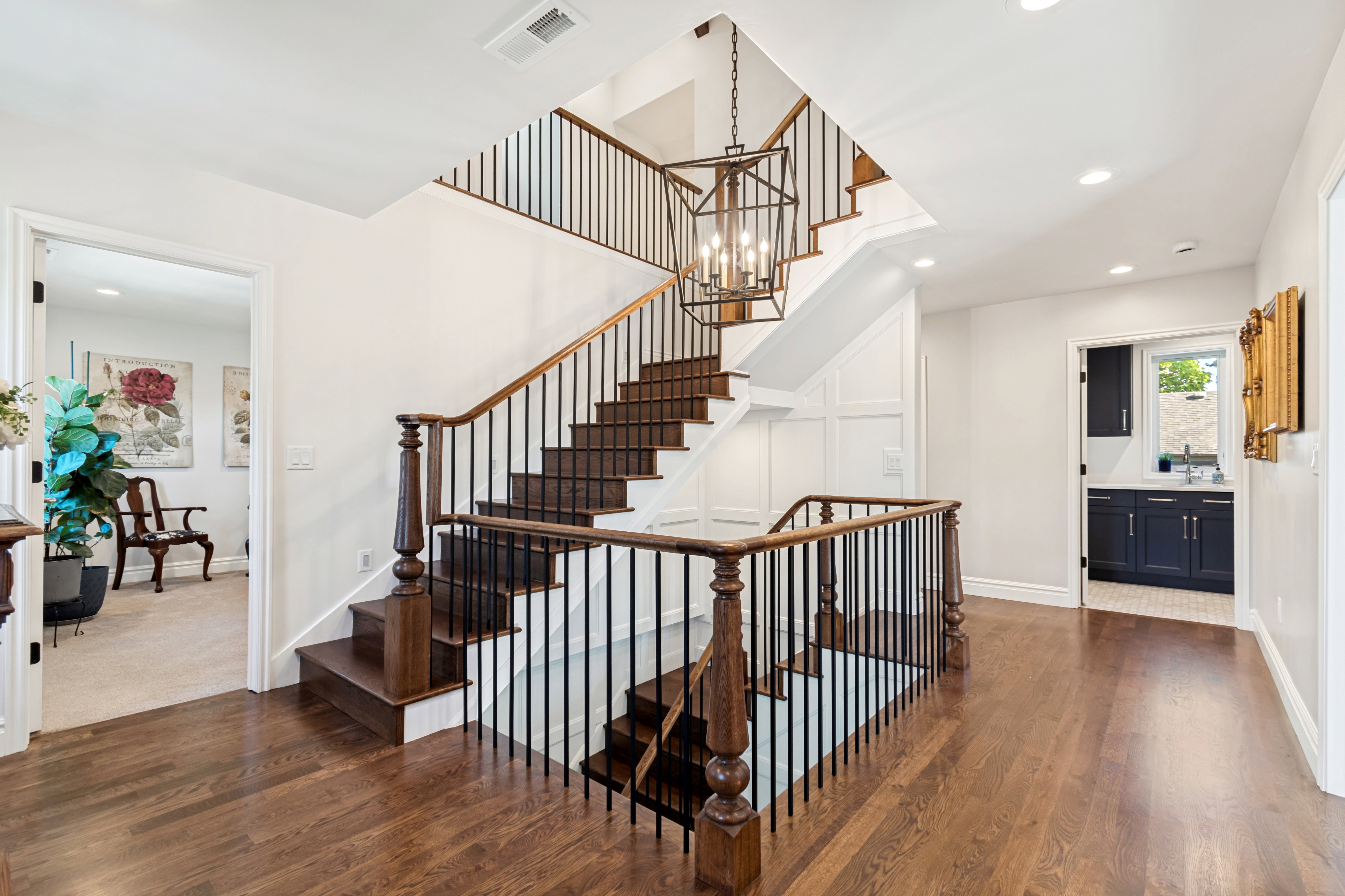 Hardwood flooring throughout the upper landing, featuring a grand staircase with dark wood treads and wrought iron balusters