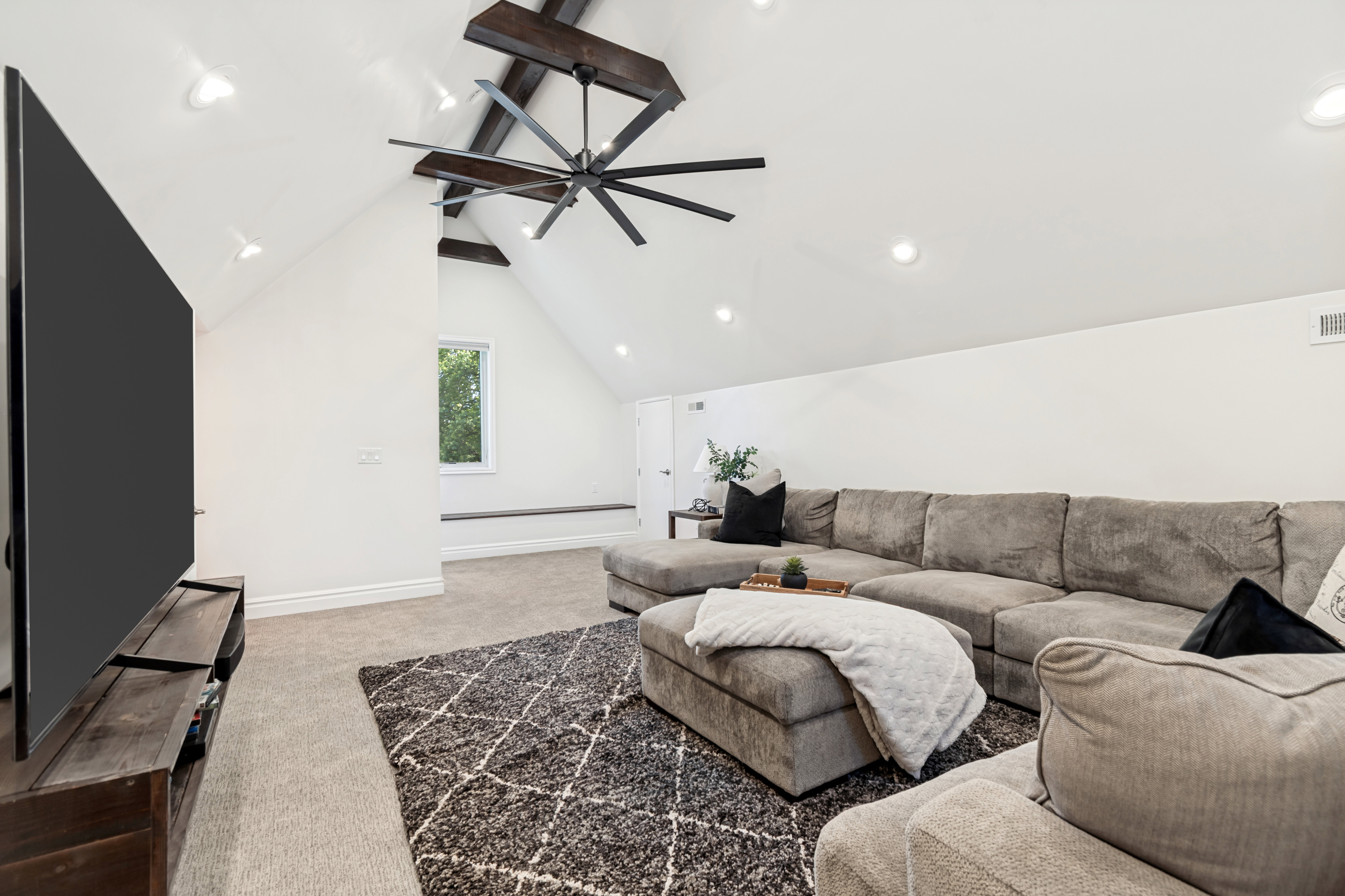 Vaulted ceiling featuring exposed wood beams and a large ceiling fan