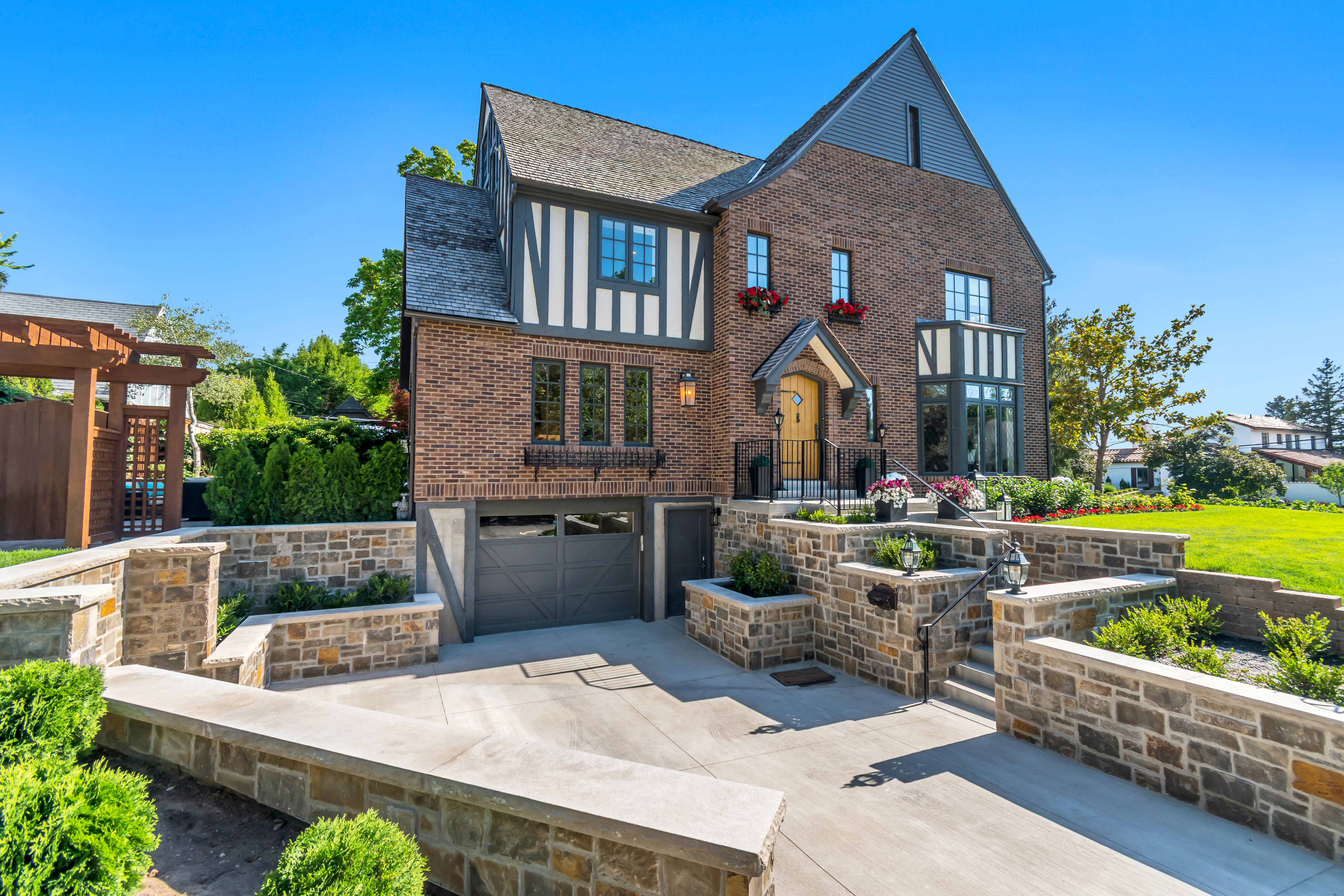 Tudor-style residence featuring a brick facade with half-timbering, a multi-level stone retaining wall system, and a paver driveway