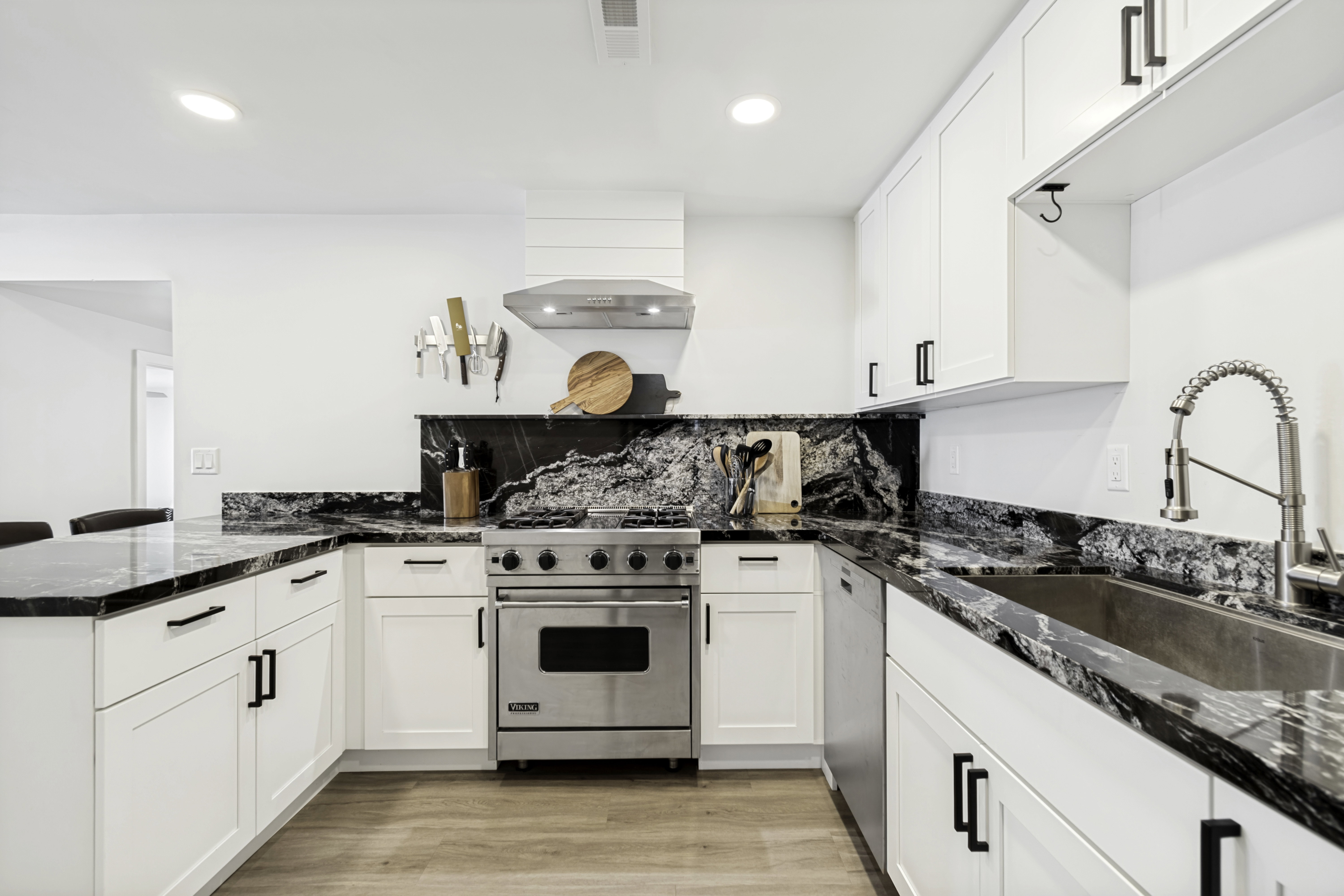U-shaped kitchen featuring white shaker cabinetry with matte black hardware, black and white patterned countertops, stainless steel appliances, and wood-finish flooring