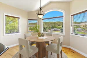 Dining area featuring an arched picture window, additional rectangular windows with blinds, wood-finish flooring, and a decorative pendant light fixture. Virtually staged.