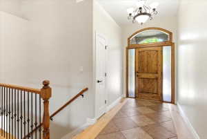 Foyer featuring a wood-finish entry door with arched transom and sidelights, overhead chandelier, and patterned tile flooring