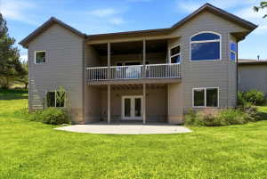 Rear exterior with a spacious concrete patio, a covered upper-level balcony with white railings, and a large arched window