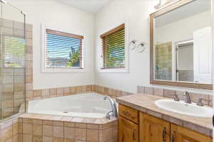 Bathroom featuring a corner soaking tub with tile surround, a glass-enclosed shower, wood-finish vanity with an undermount sink, and a framed mirror