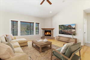 Vaulted ceilings highlight this living space, featuring a stone-clad fireplace with a wood mantle, blonde wood-finish flooring, and a triple window assembly with horizontal blinds.Virtually staged.