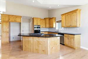 Kitchen featuring light wood cabinetry, dark countertops, a central island with a built-in cooktop, light wood-finish flooring, and recessed lighting