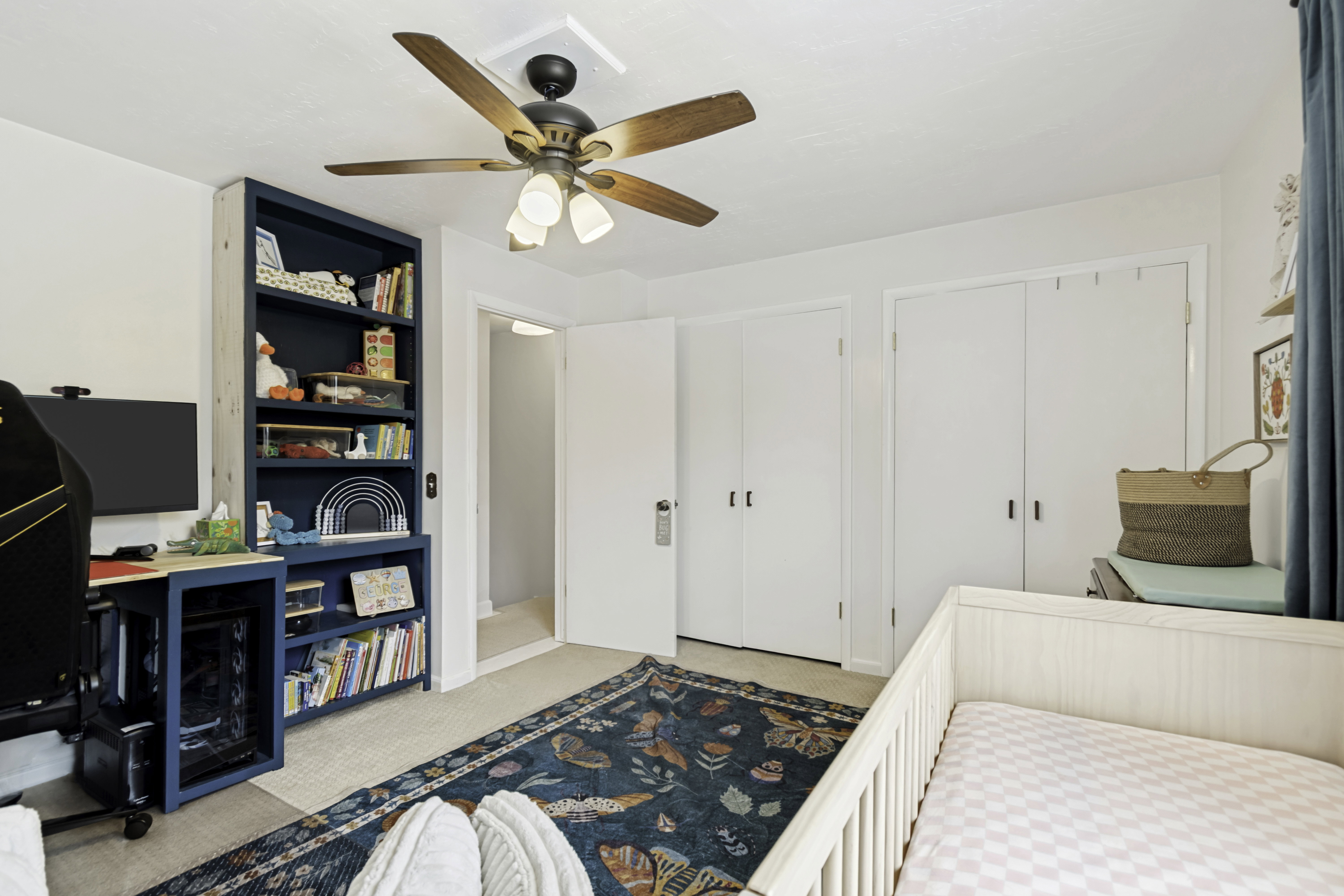 Carpeted interior space featuring a ceiling fan with integrated lighting, built-in shelving, and two sets of bi-fold closet doors