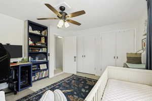 Carpeted interior space featuring a ceiling fan with integrated lighting, built-in shelving, and two sets of bi-fold closet doors