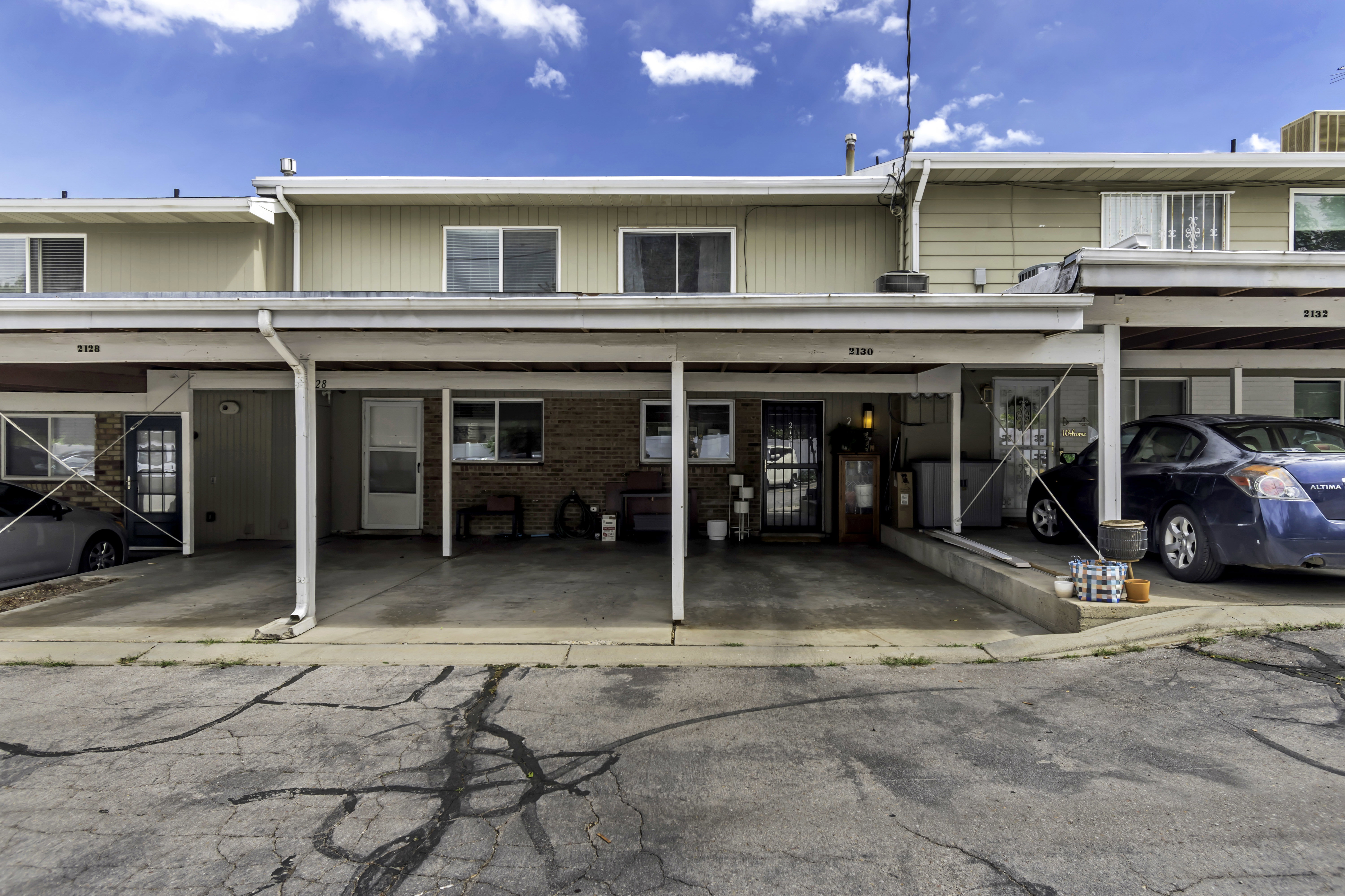 Townhome exterior featuring individual carports, upper-level windows, and a brick facade on the lower level