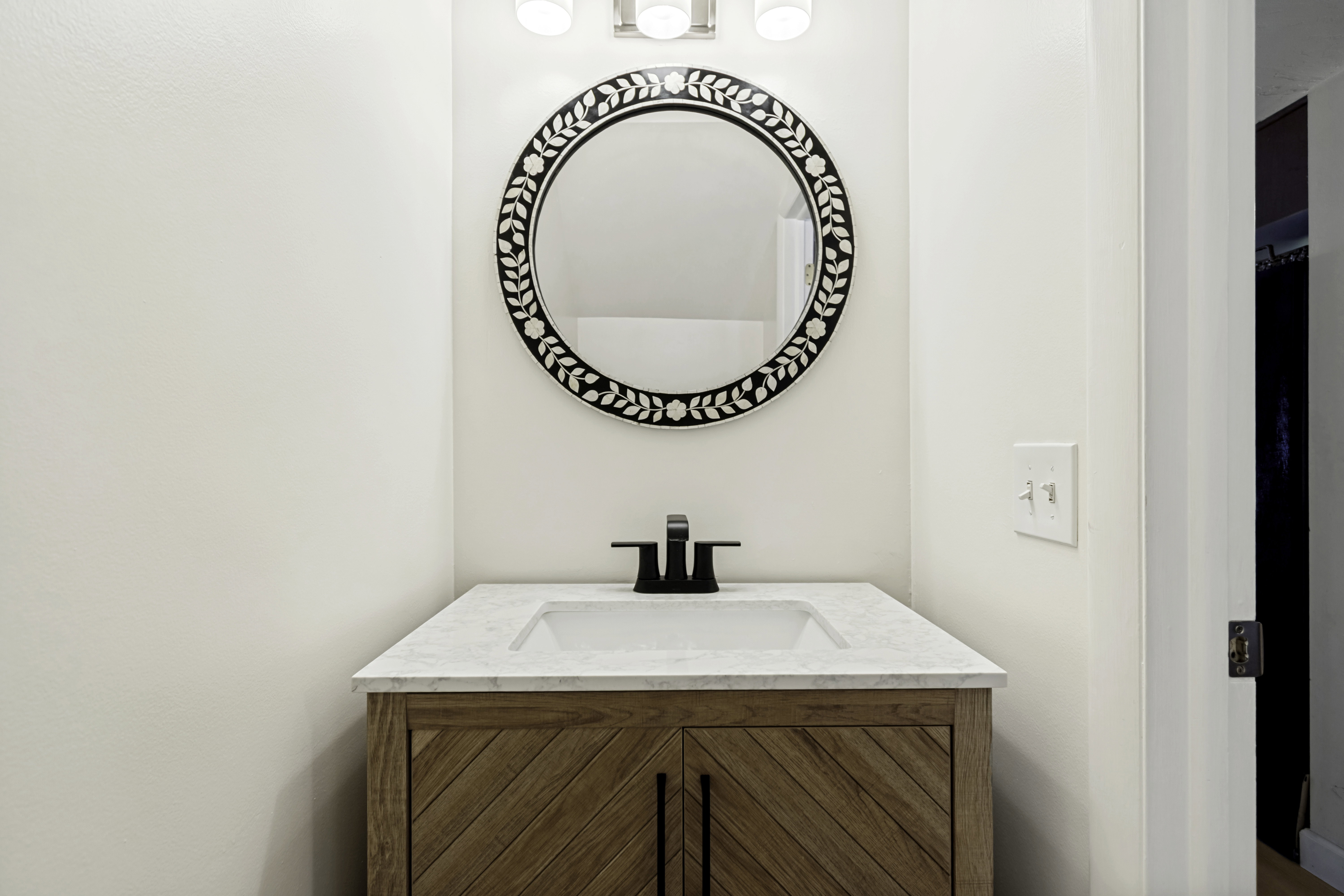 Modern vanity featuring a patterned wood-finish cabinet with black hardware, a light-toned countertop with integrated sink, and a matte black faucet
