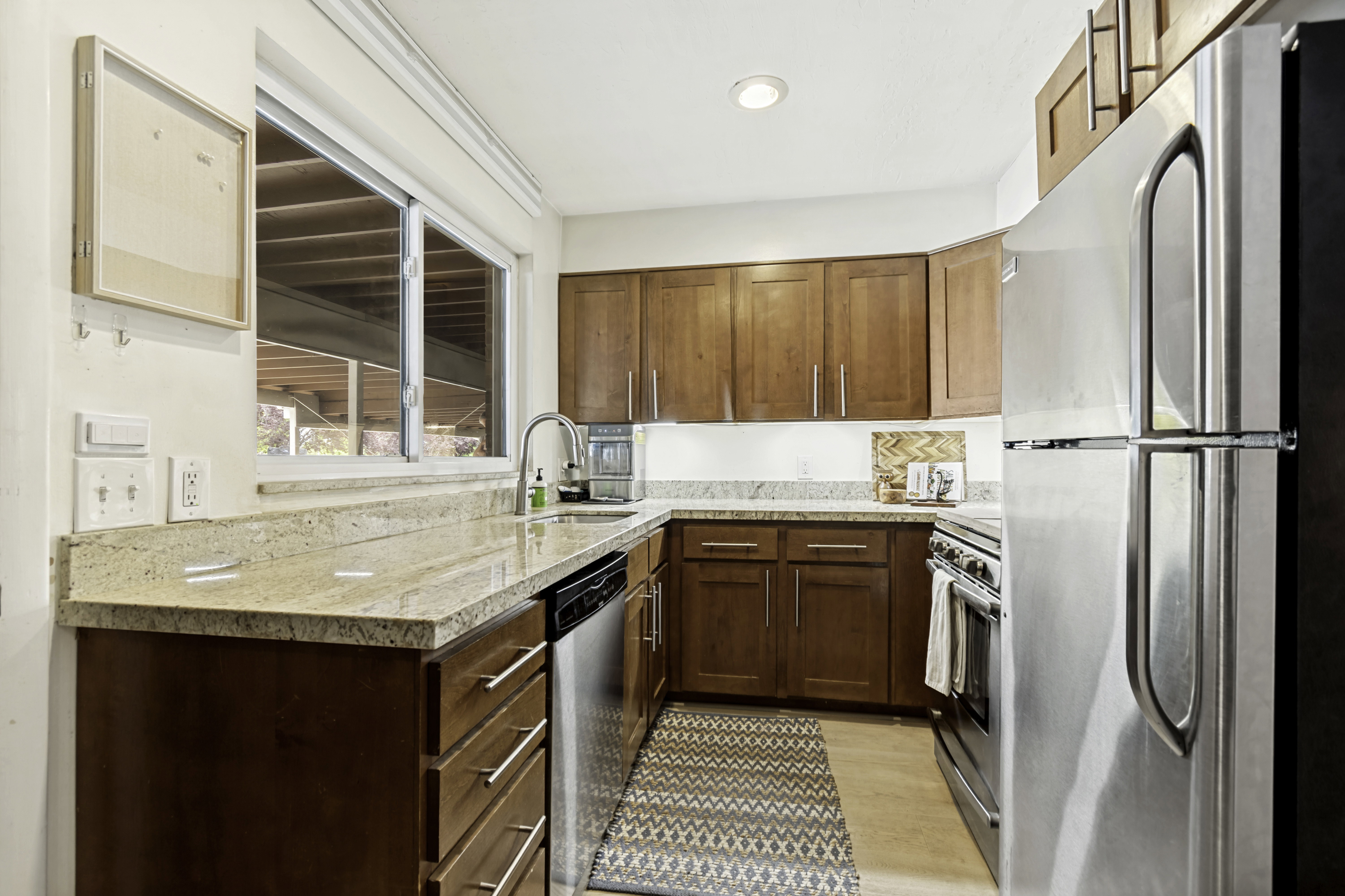 Kitchen featuring wood-finish cabinetry, granite-style countertops, stainless steel appliances, a stainless steel sink with a gooseneck faucet, and light wood-finish flooring