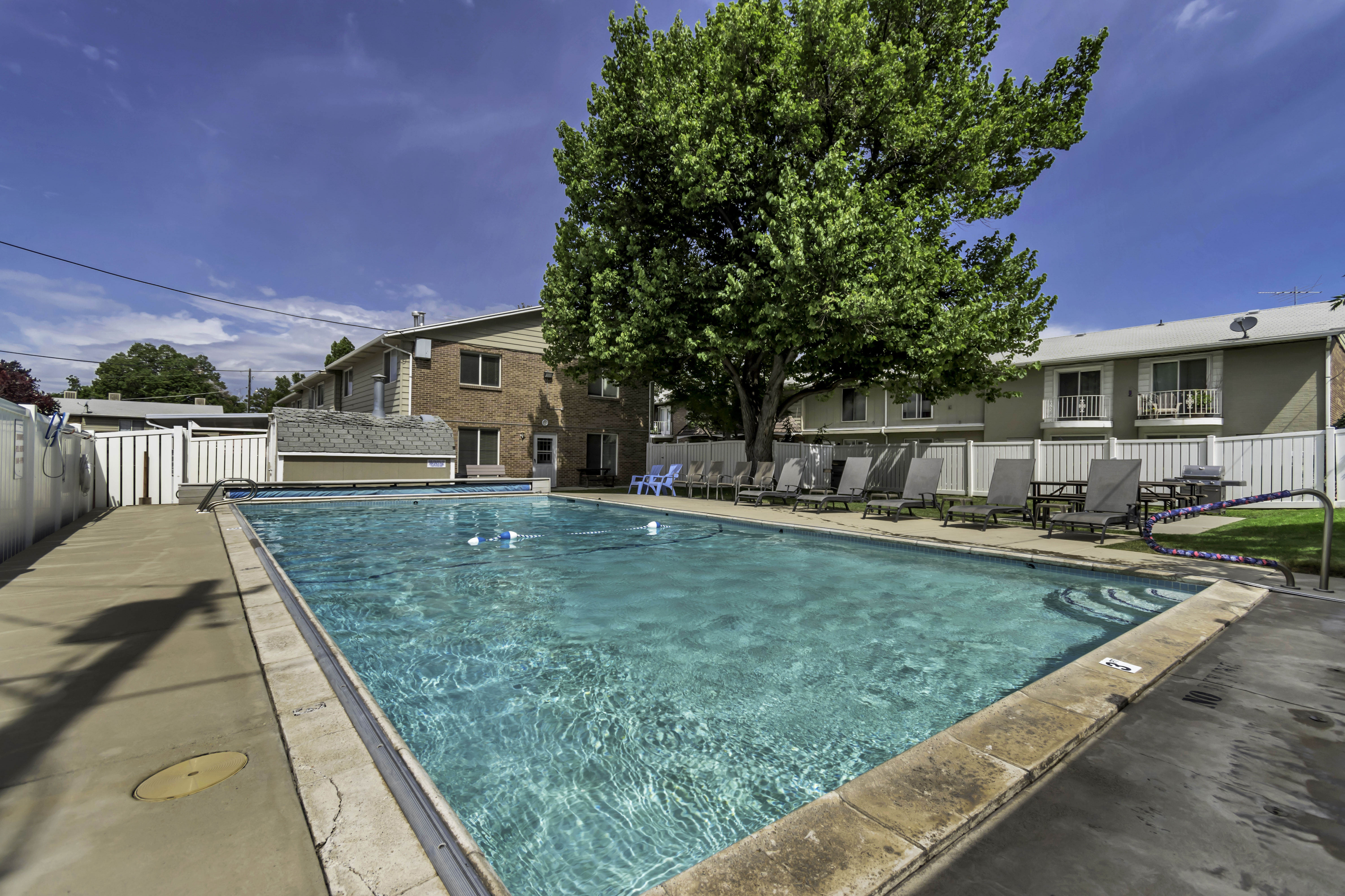Outdoor swimming pool with concrete decking, surrounding privacy fencing, and lounge seating