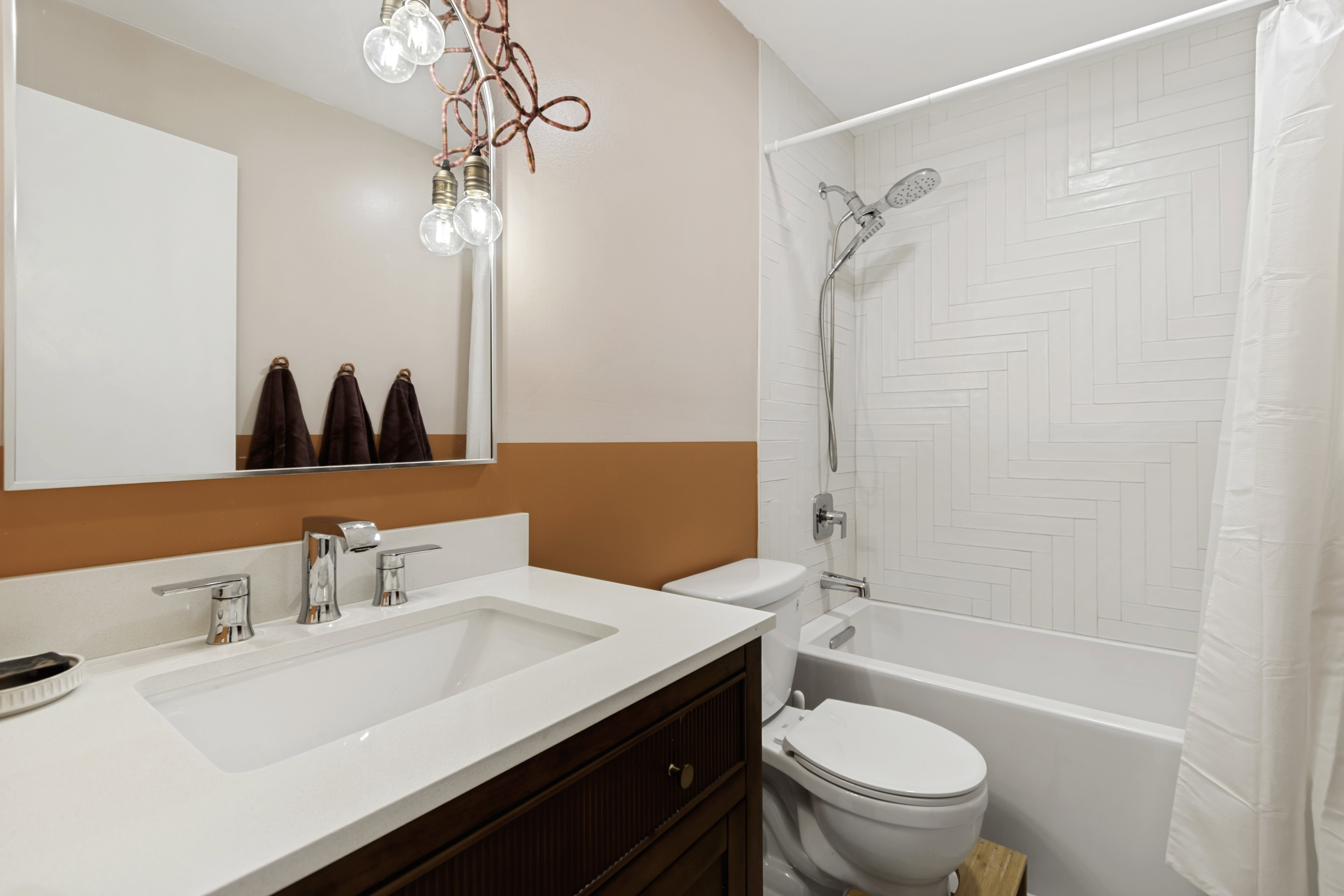Bathroom featuring a white integrated sink with chrome fixtures, a wood-finish vanity, and a mirror with an exposed bulb light fixture