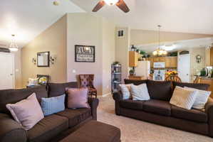 Living area featuring an open concept design with vaulted ceilings, a ceiling fan, and carpet flooring
