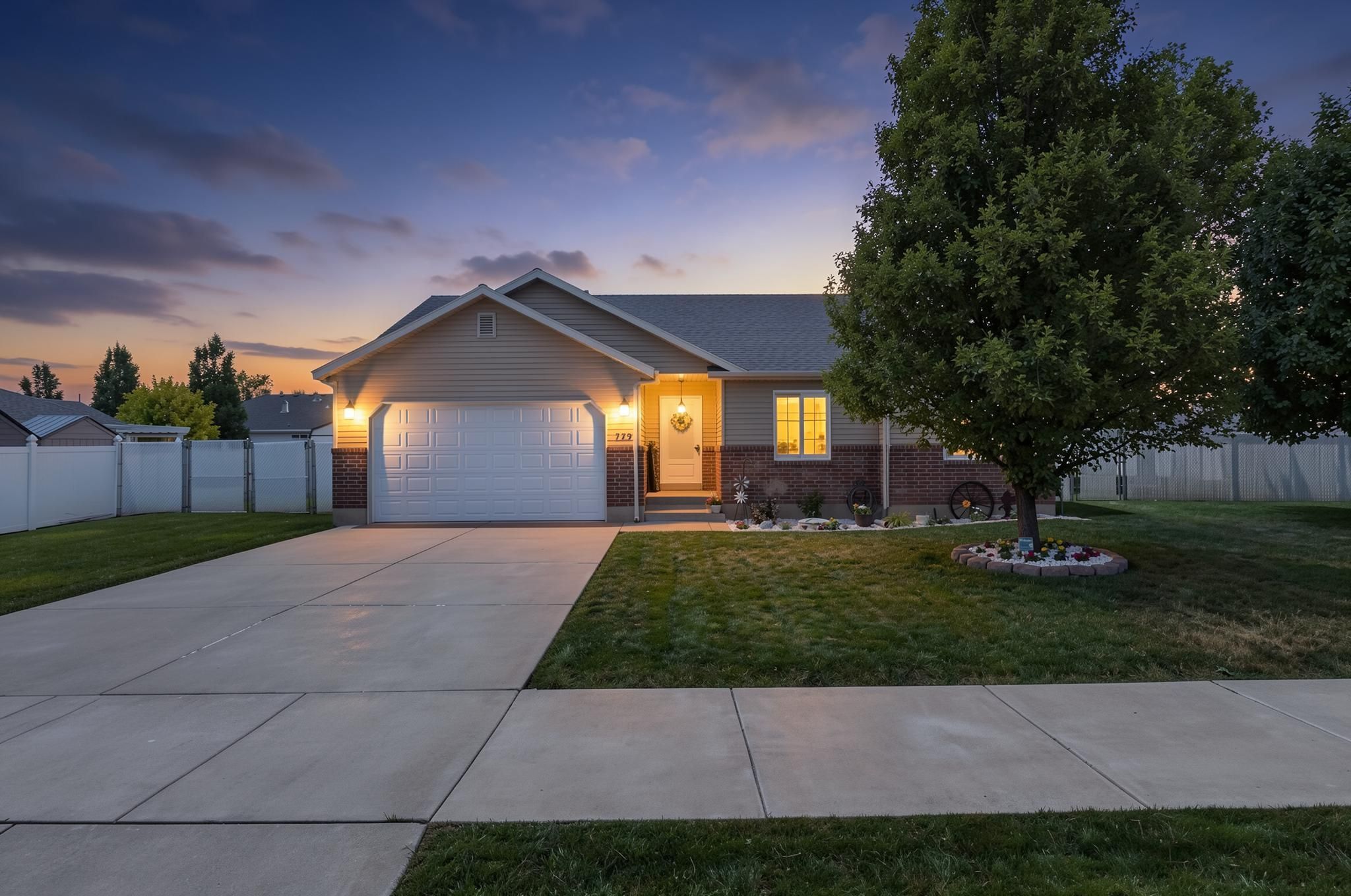 Ranch-style residence featuring a two-car garage, brick and siding exterior, a concrete driveway, a manicured lawn, and mature trees