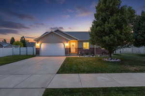 Ranch-style residence featuring a two-car garage, brick and siding exterior, a concrete driveway, a manicured lawn, and mature trees
