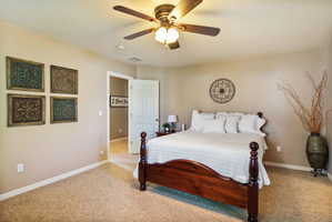 Master bedroom featuring a ceiling fan with integrated lighting, neutral wall tones, white trim, and a white interior door