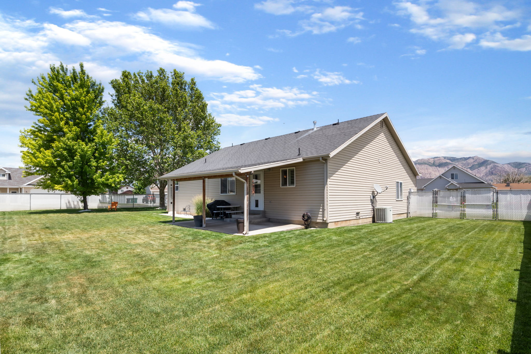 Expansive backyard featuring a covered patio, manicured lawn, mature trees, and privacy fencing