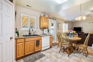 Kitchen featuring wood-finish cabinetry, granite-style countertops, a black sink with a black faucet, and a white dishwasher