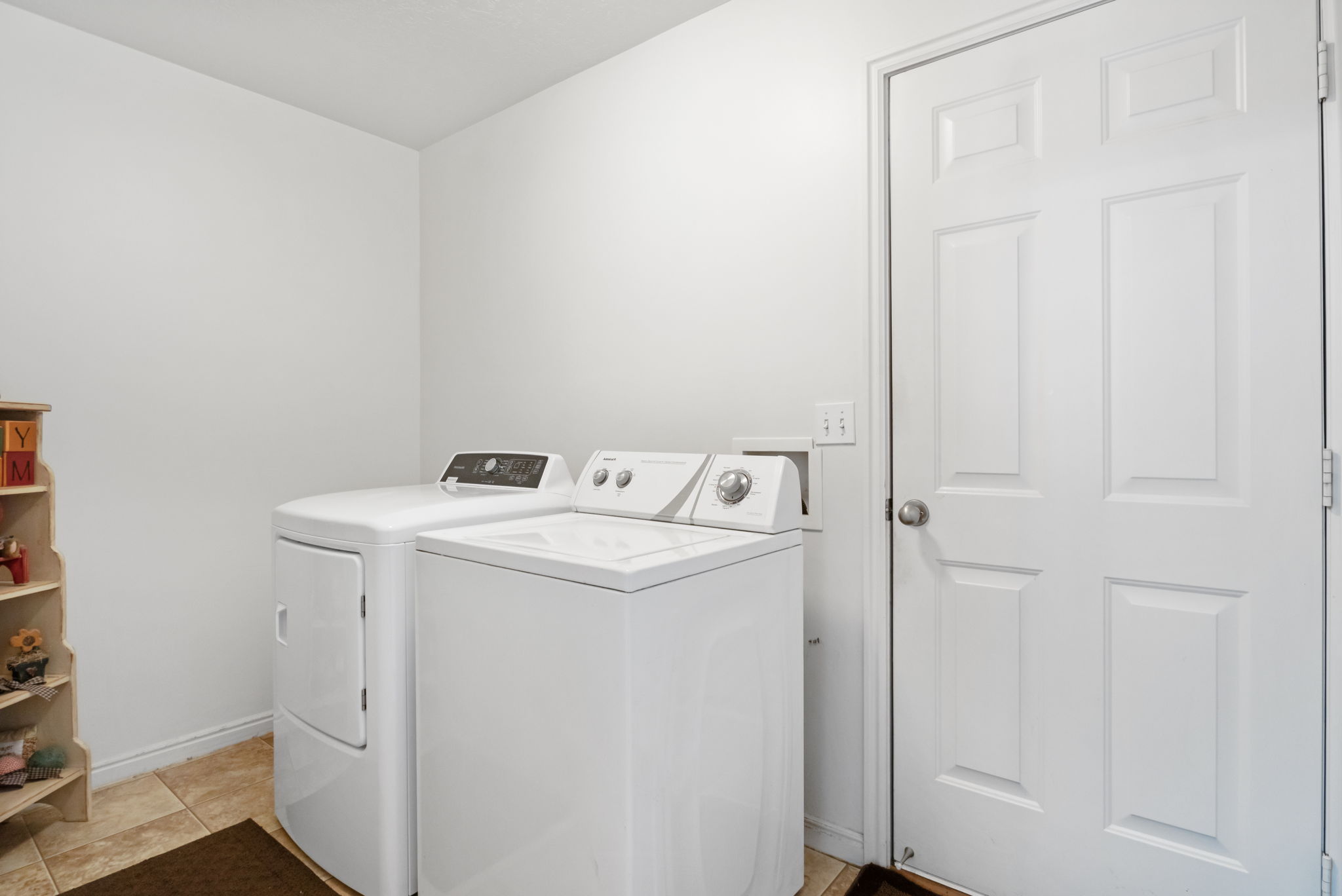 Dedicated laundry space with neutral tile flooring, white walls, and a paneled door