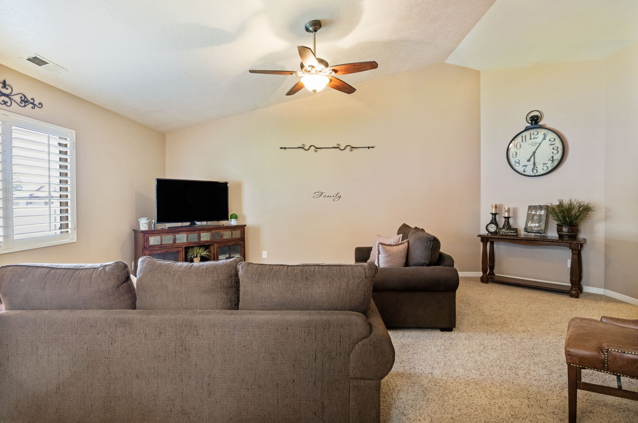 Living area with vaulted ceilings, plantation shutters, and a ceiling fan with integrated lighting