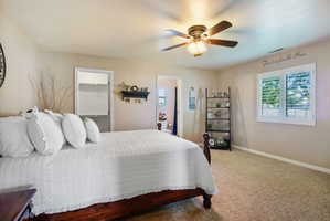 Master bedroom featuring a ceiling fan with light fixture, window with white plantation shutters, and a closet with built-in shelving