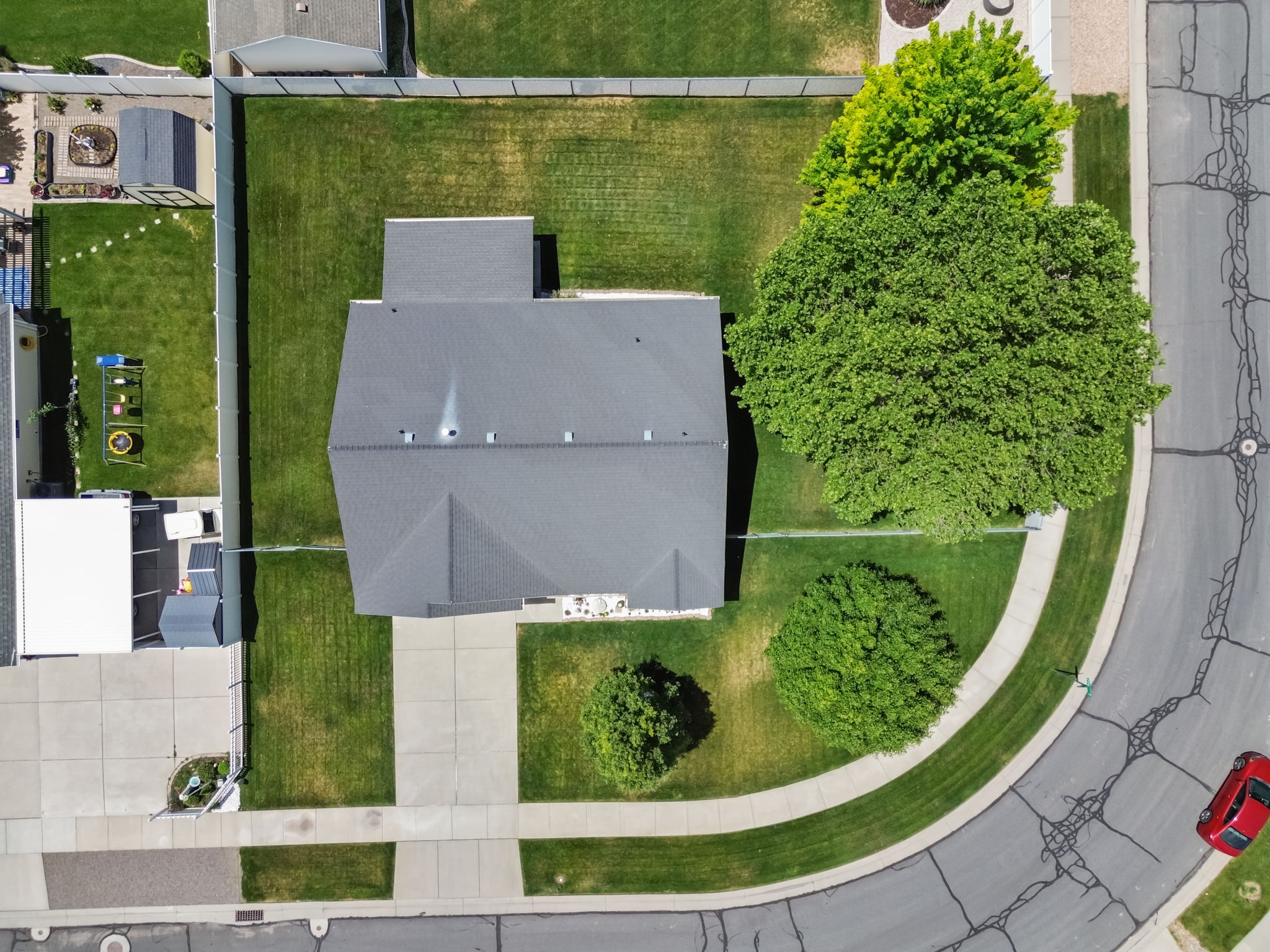 Aerial view of a residential property featuring a gray shingled roof, a paved driveway, and established trees