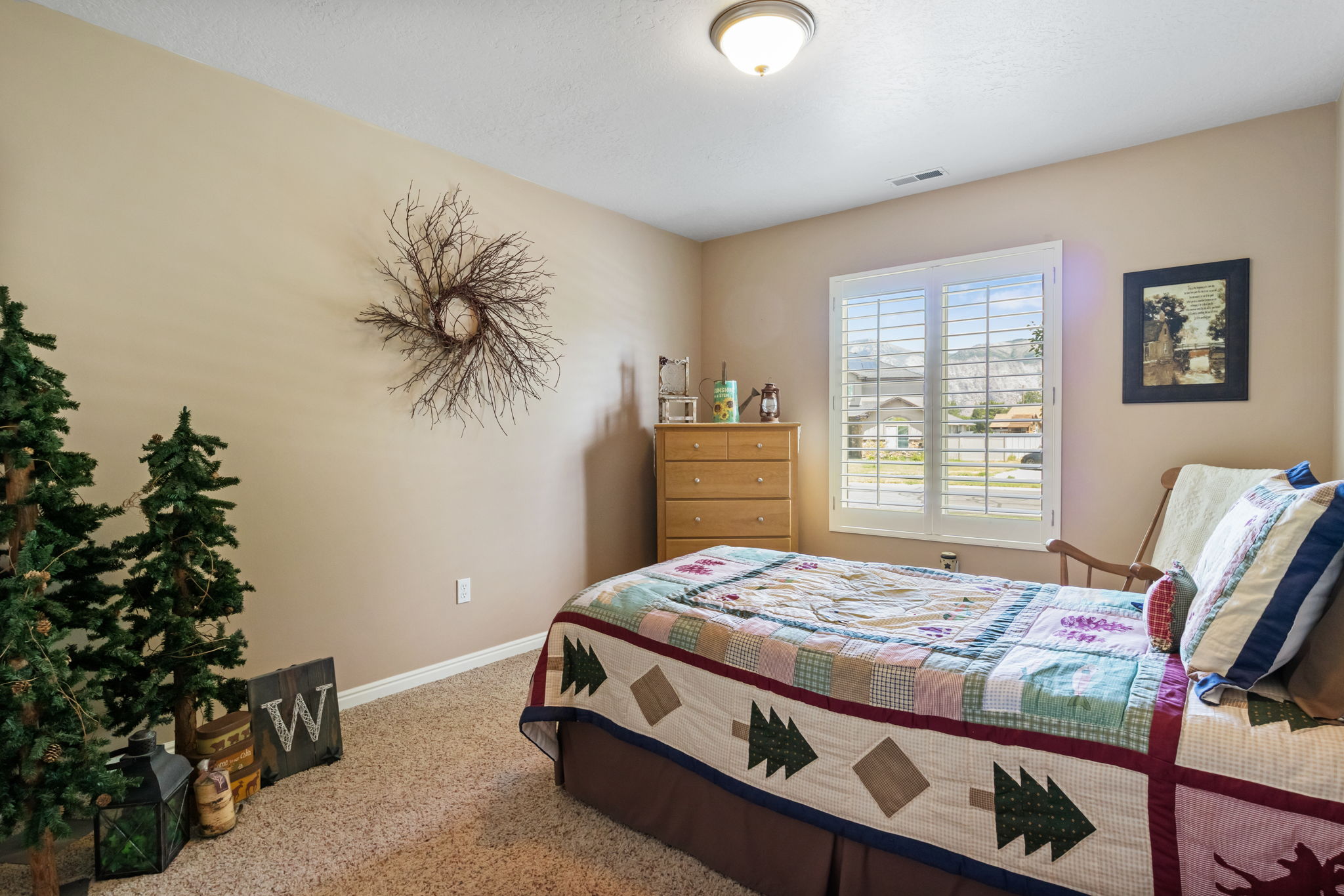 Guest bedroom featuring neutral wall paint, textured carpet flooring, a window with plantation shutters, and a flush-mount ceiling light
