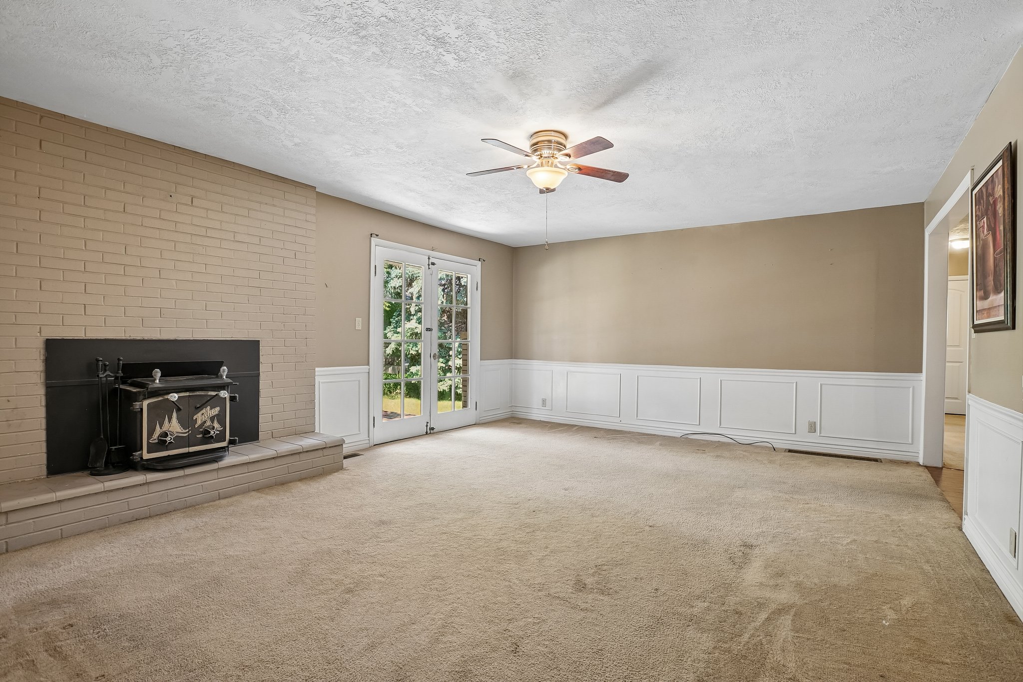 Living area featuring a brick-surround fireplace with a wood-burning insert, framed by white French doors opening to outdoor space