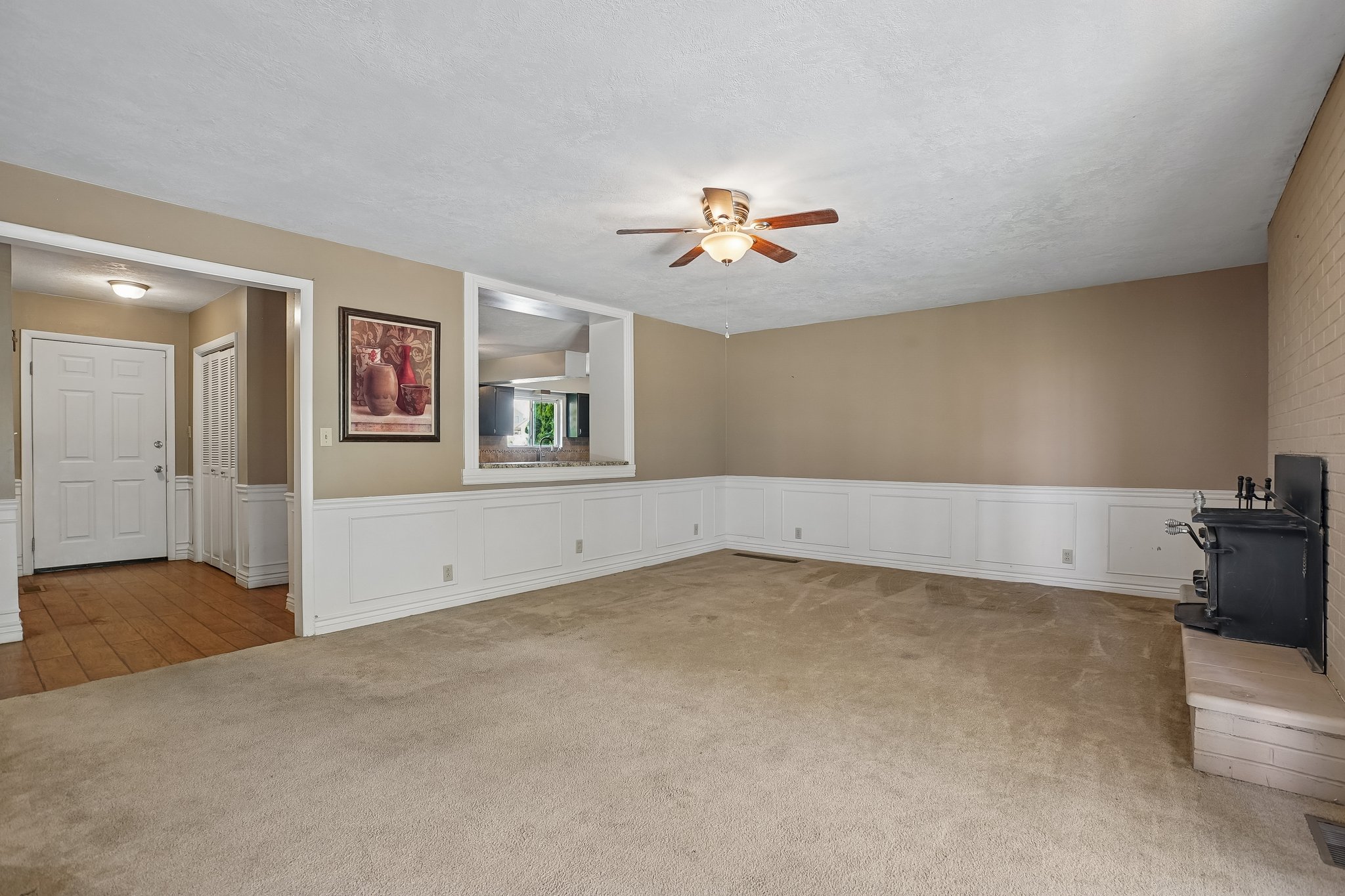 Carpeted living area featuring wainscoting, a ceiling fan with light fixture, and a brick fireplace with a hearth