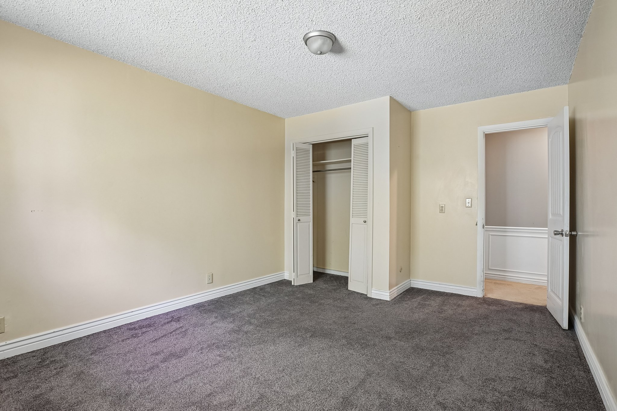 Carpeted room featuring a ceiling-mounted light fixture, bi-fold closet doors, and light-toned wall paint with white baseboards