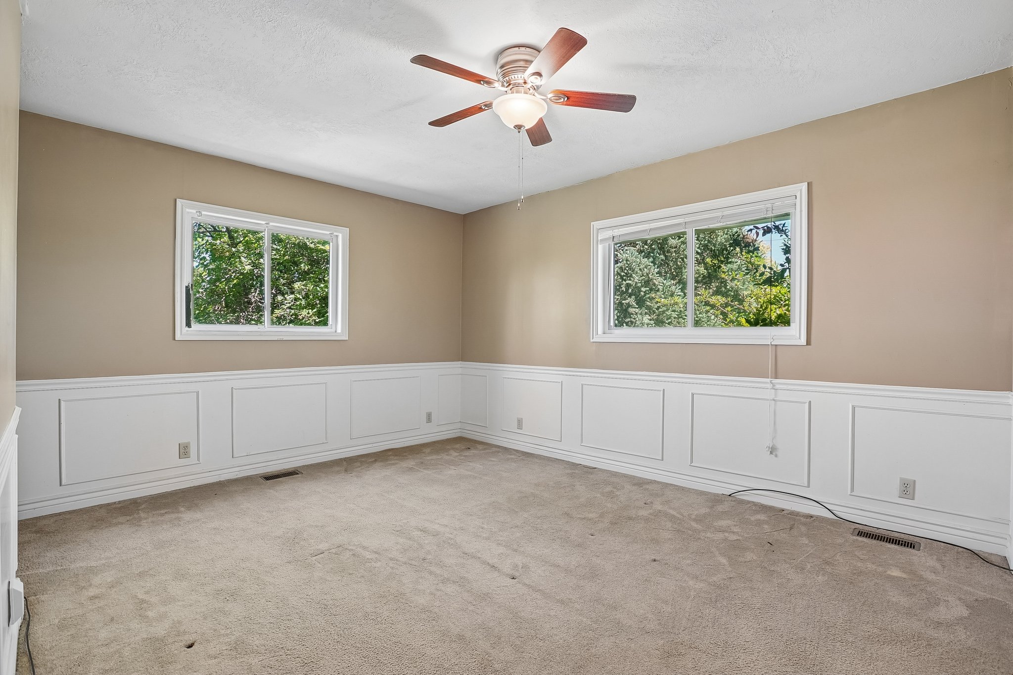 Spacious room featuring neutral carpeting, chair rail molding, and two windows offering exterior views