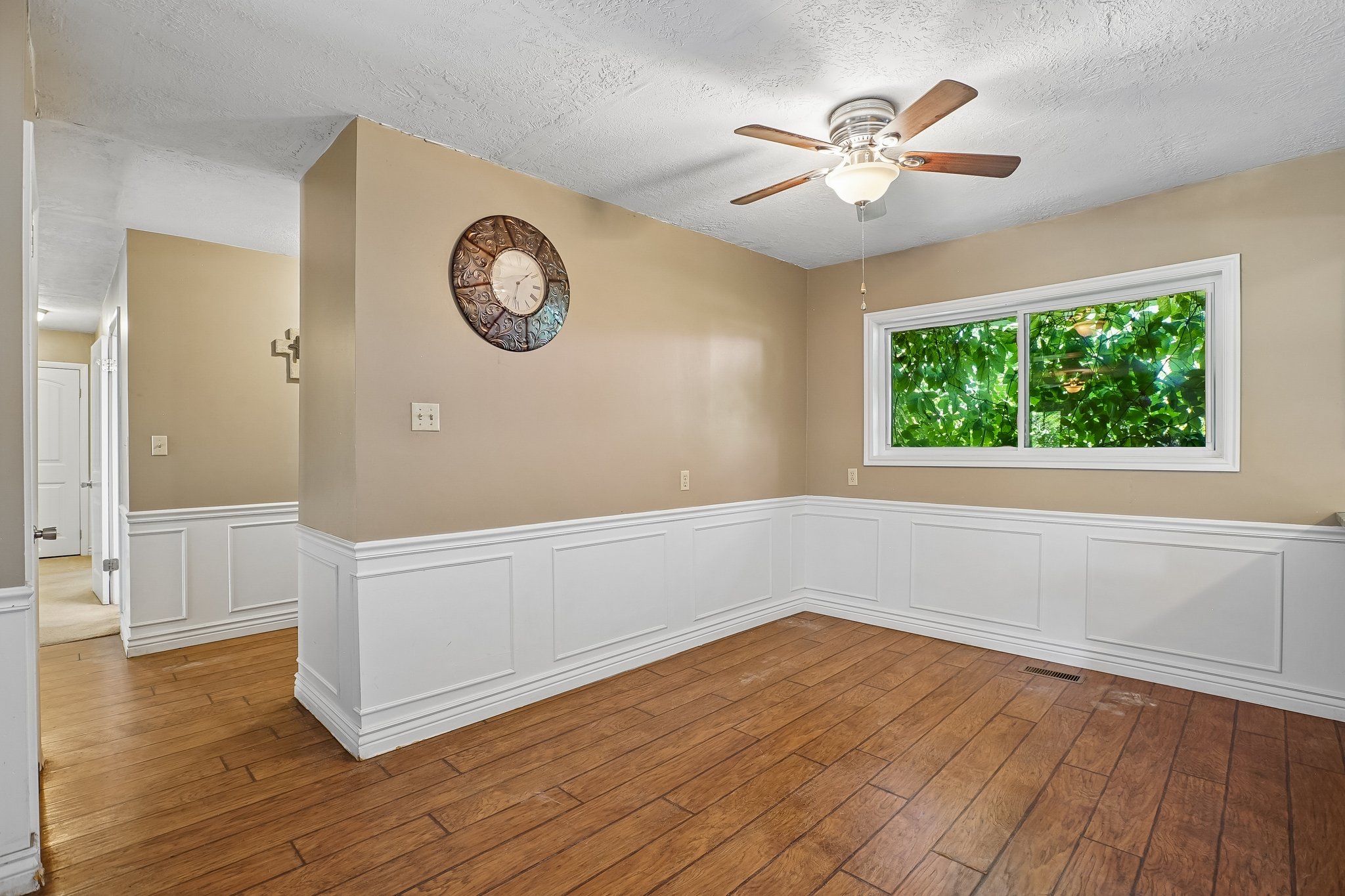 Interior room featuring wood-finish flooring, wainscoting, and a window with green foliage visible
