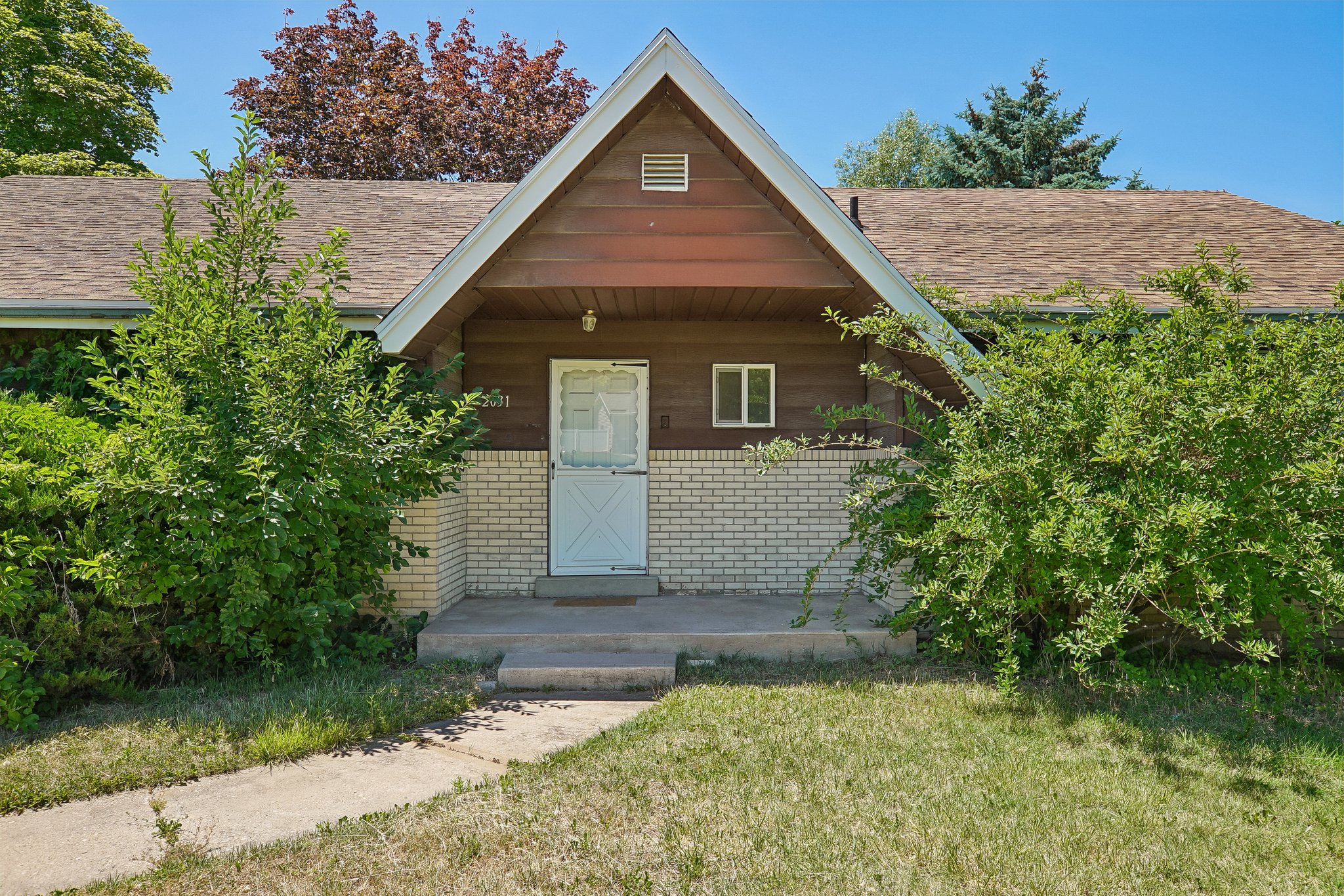 Gable-front home featuring a covered entry, light-colored brick facade, wood siding, and mature landscaping