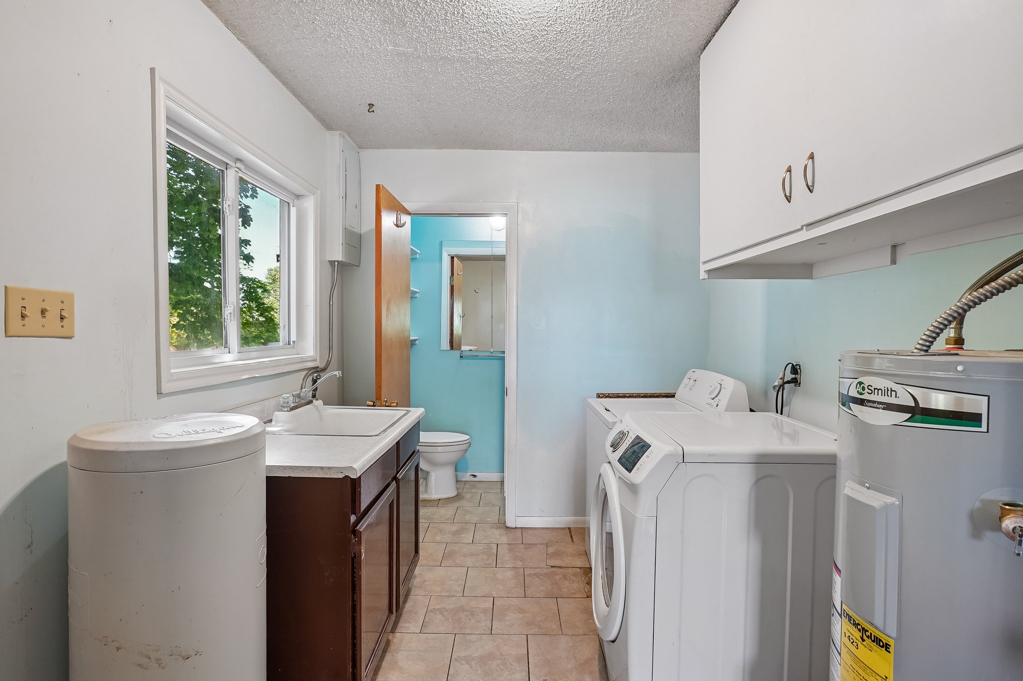Utility room featuring a window, built-in sink with cabinetry, and tiled flooring