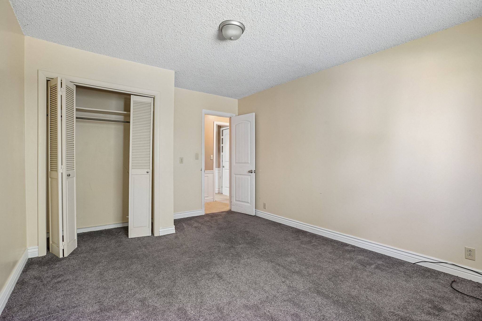 Spacious room featuring gray carpet flooring, light cream wall paint, and white baseboards