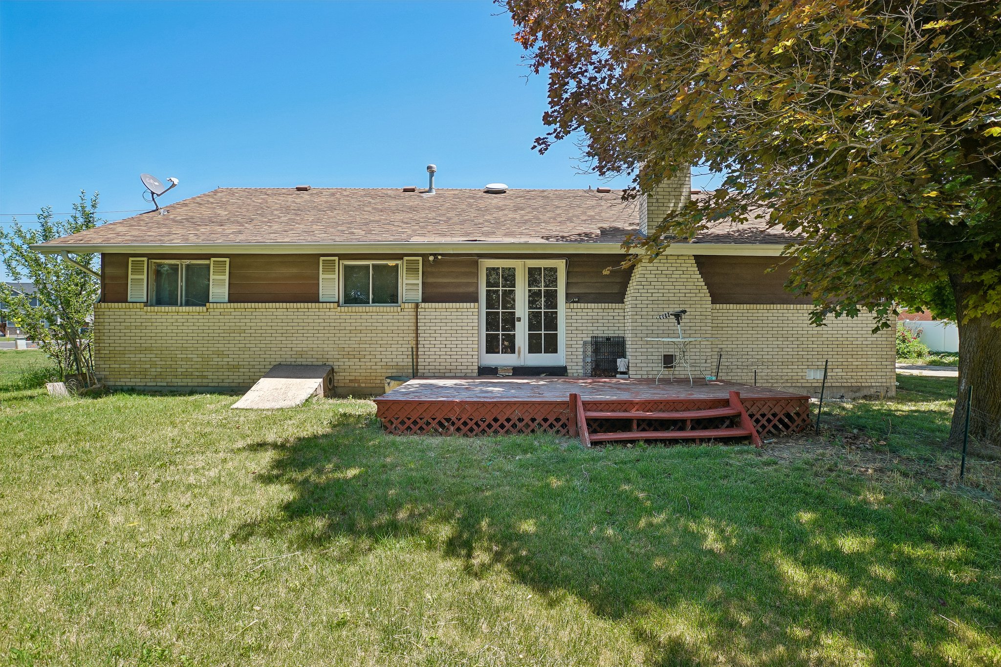 Rear exterior featuring a spacious wooden deck with lattice detailing, double French doors, and a light-colored brick facade