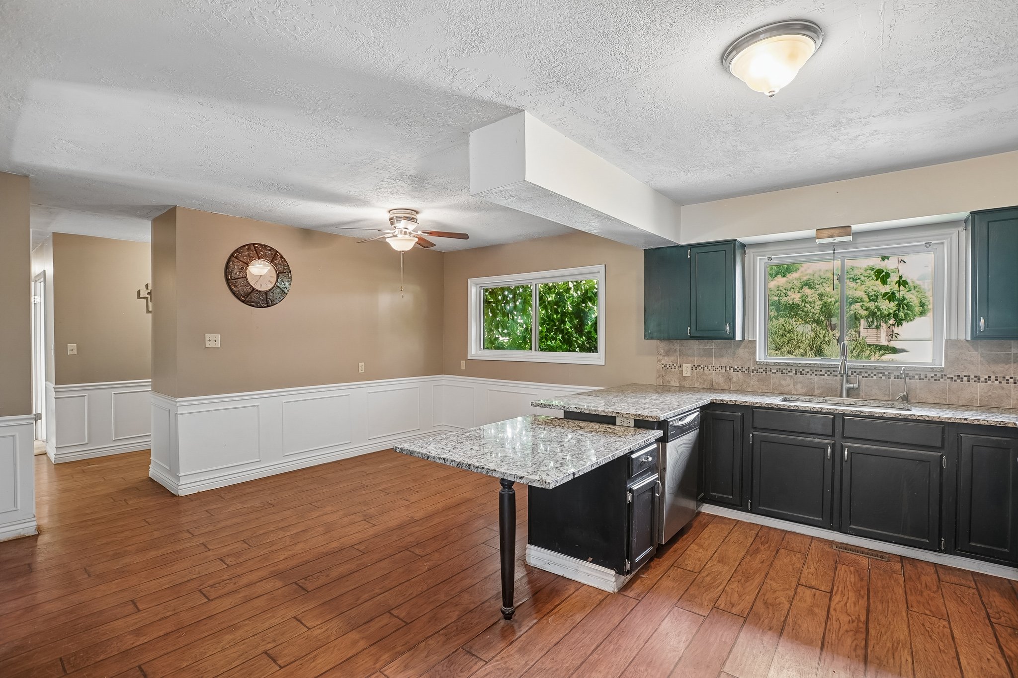 Kitchen featuring dark cabinetry with light granite-finish countertops, stainless steel dishwasher, and tile backsplash