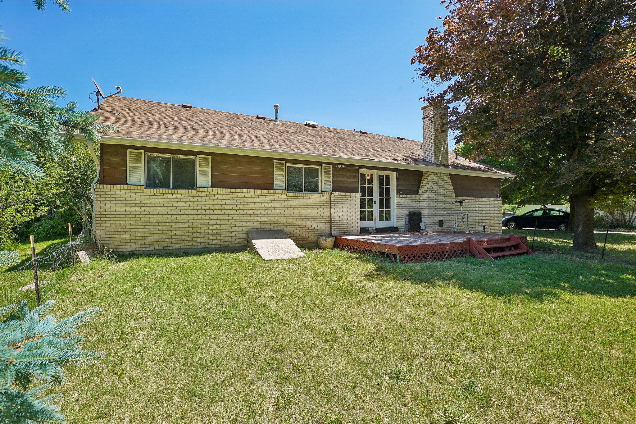 Exterior featuring a light brick facade, horizontal wood siding, a brown shingle roof, a rear wood deck with lattice detailing, and double French doors