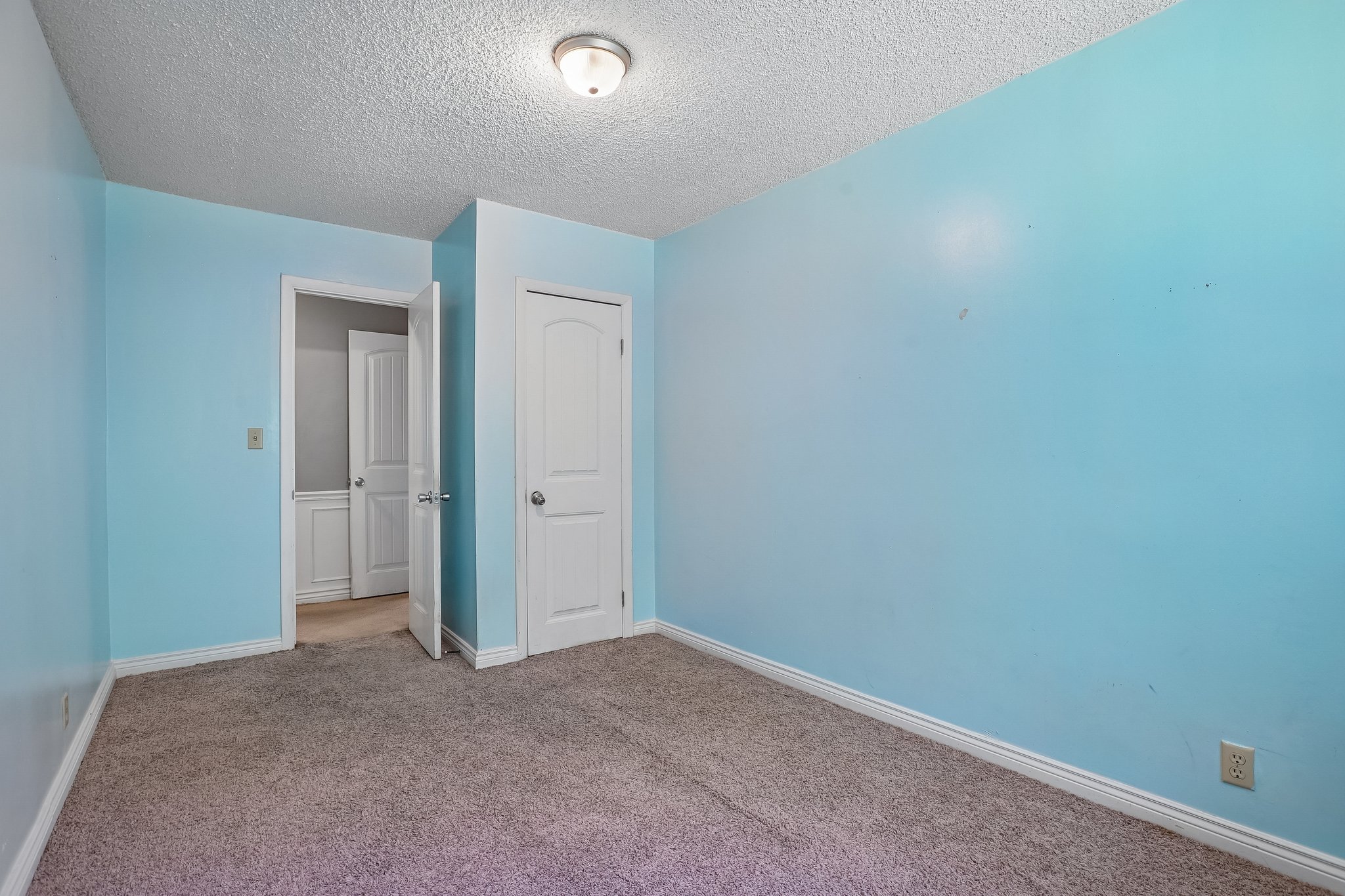Room featuring light blue walls, gray carpet, white trim, a flush mount ceiling light, and a white interior door