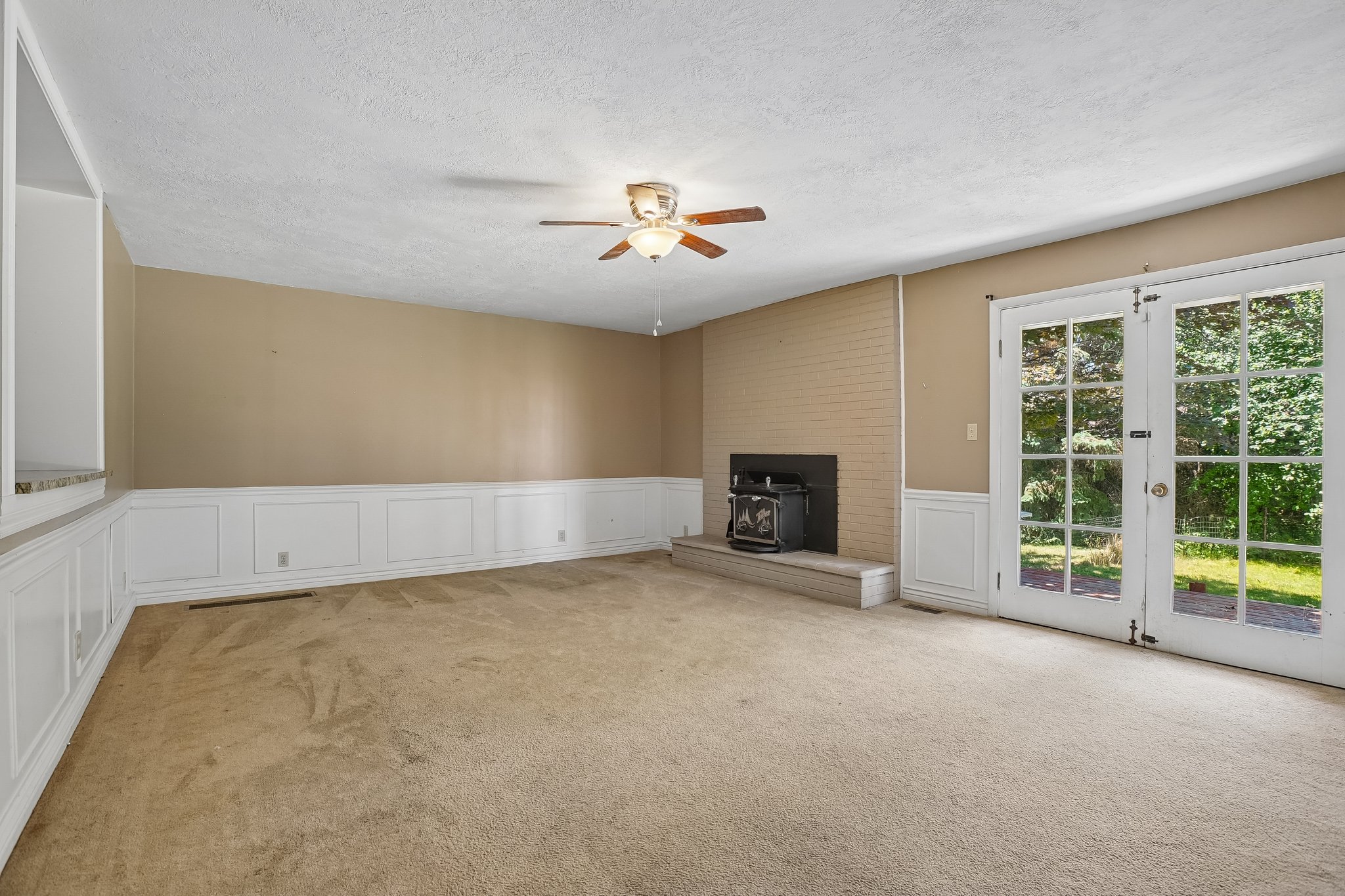 Spacious interior featuring neutral carpeting, wainscoting, and a ceiling fan